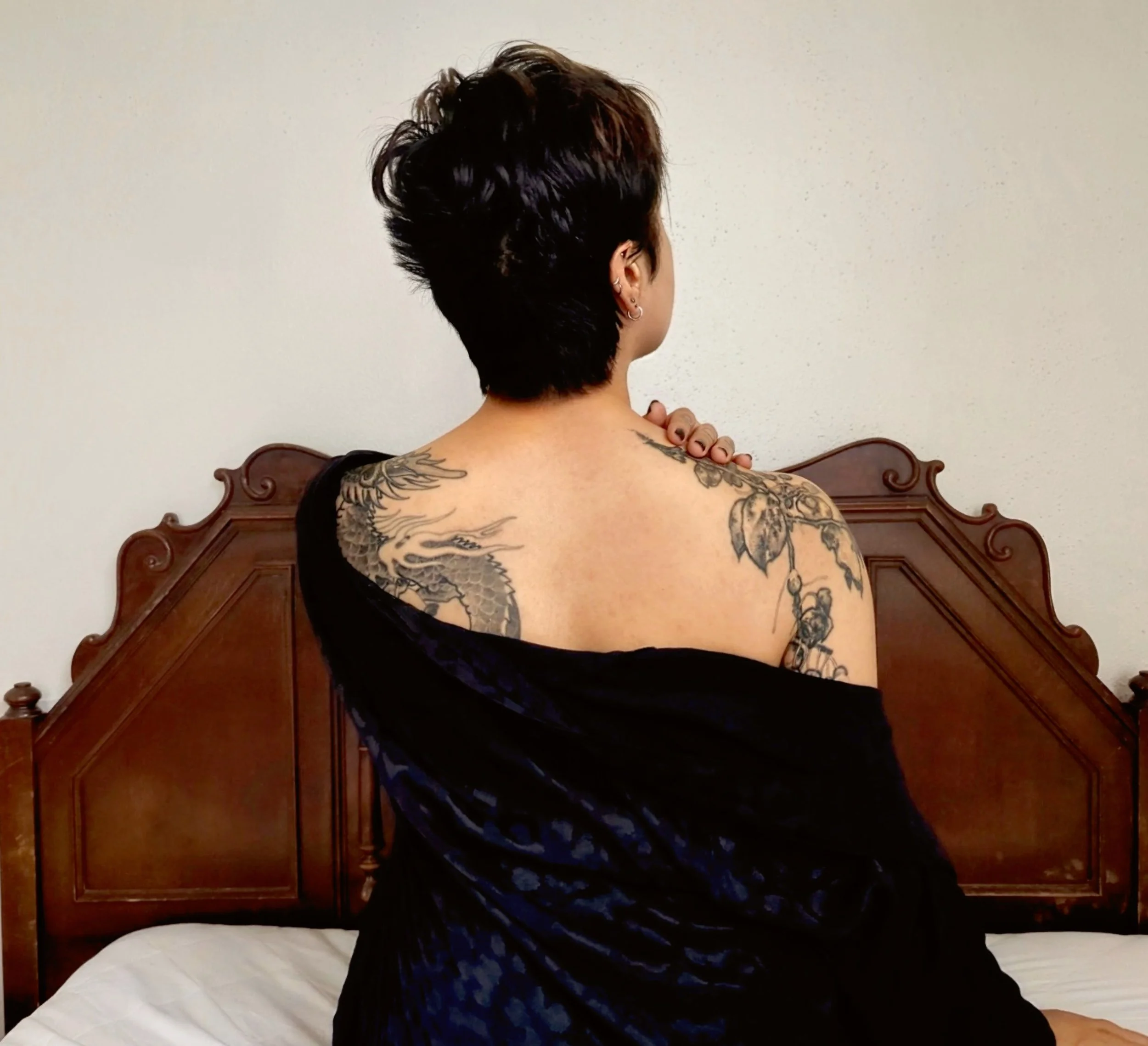 A photo of Thorne Vo's pixie cut from behind as a blue silk robe slips down over her shoulders to reveal botanical tattoos.