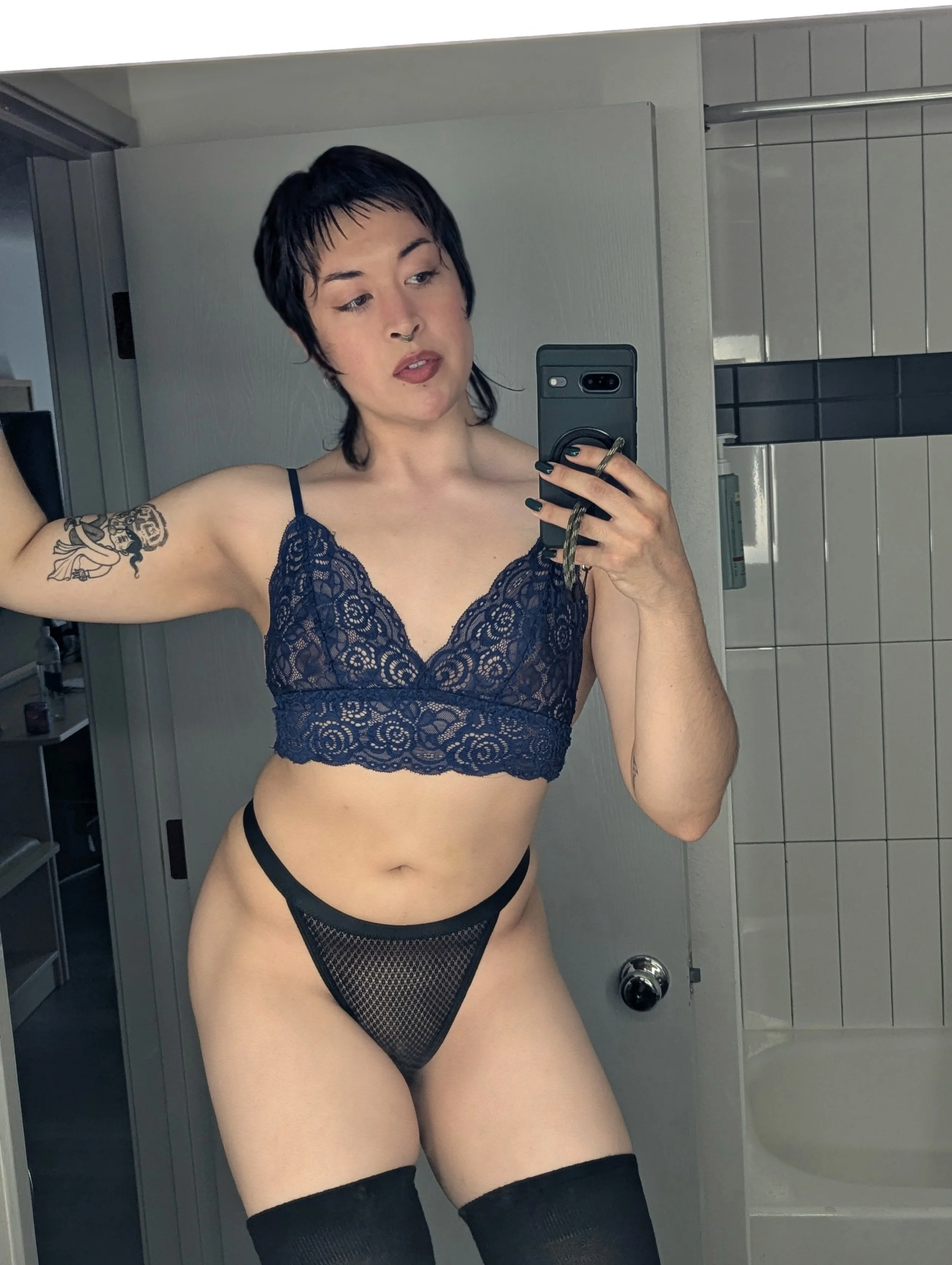 A mirror selfie of Thorne Vo wearing black stockings, black panties, and a blue lace bralette.
