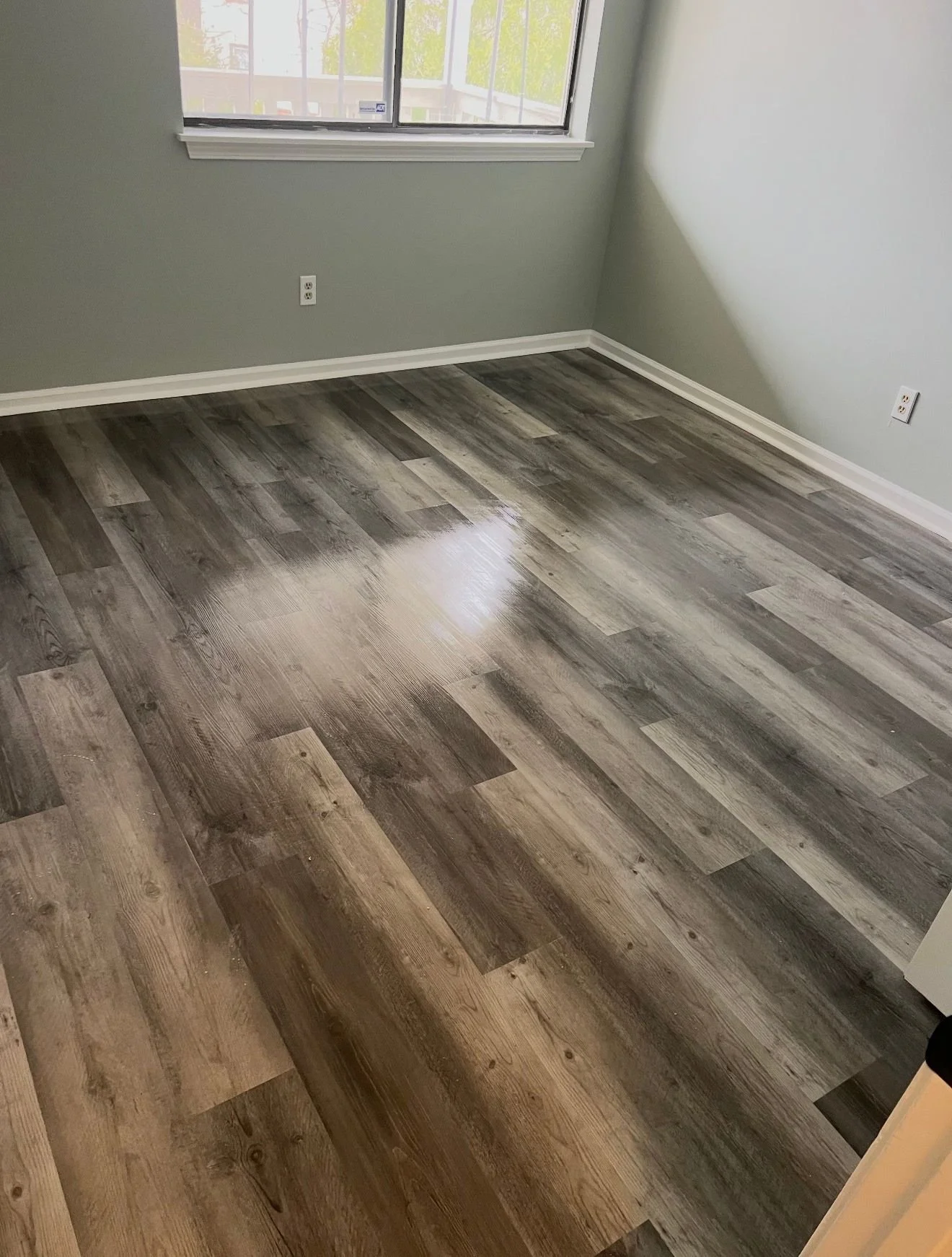 Empty room with wooden flooring, a window letting in natural light, light-colored walls, and electrical outlets.
