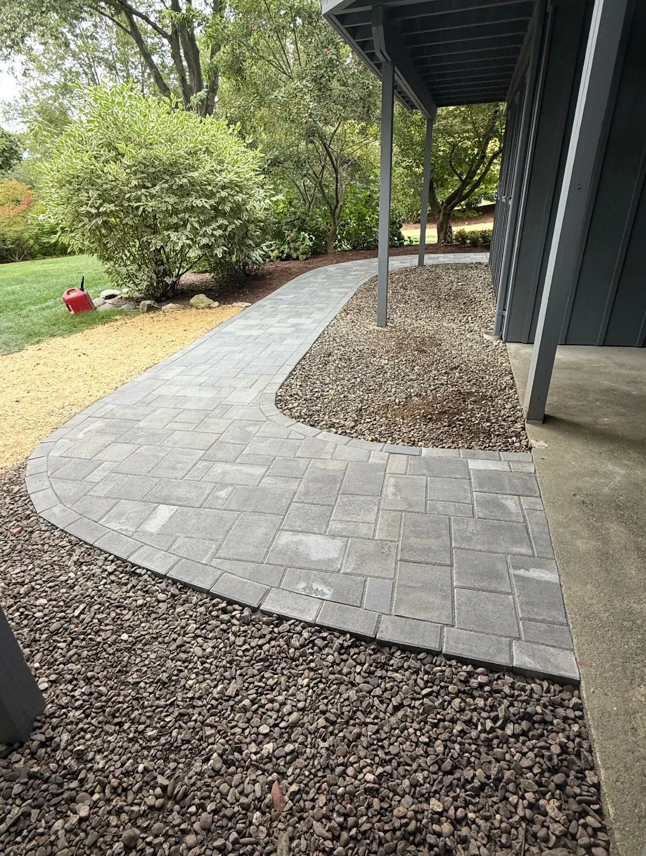 A curved gray brick walkway bordered by small rocks and landscaping, with trees and a lawn in the background.
