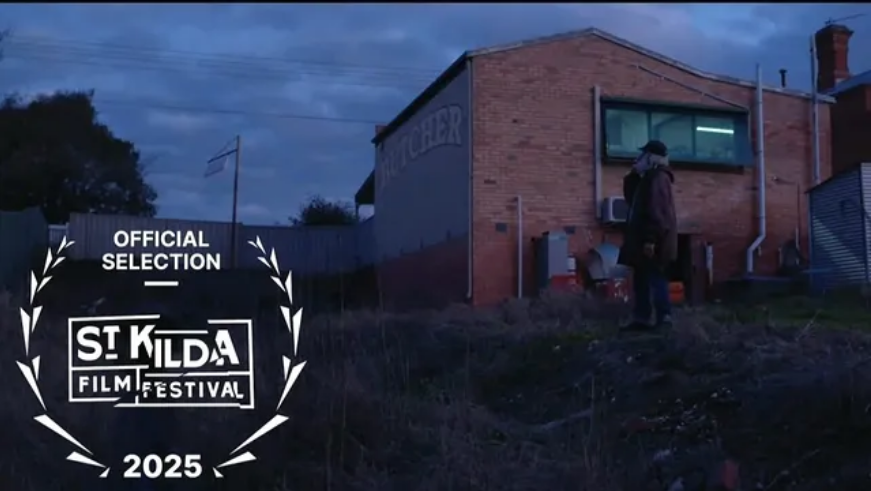 A person standing outside a brick building with a window and a sign that reads 'CHARCHER' at dusk, with an overlay of the St. Kilda Film Festival 2025 official selection emblem.