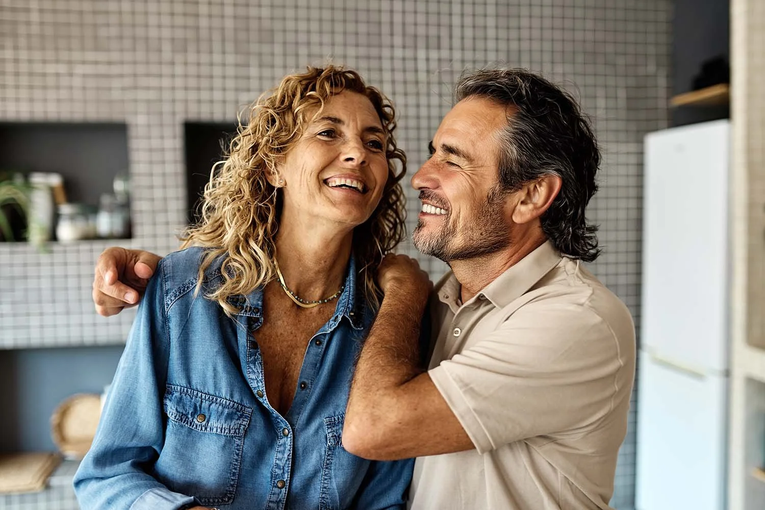 A happy middle-aged couple hugging and smiling in their Brisbane kitchen.
