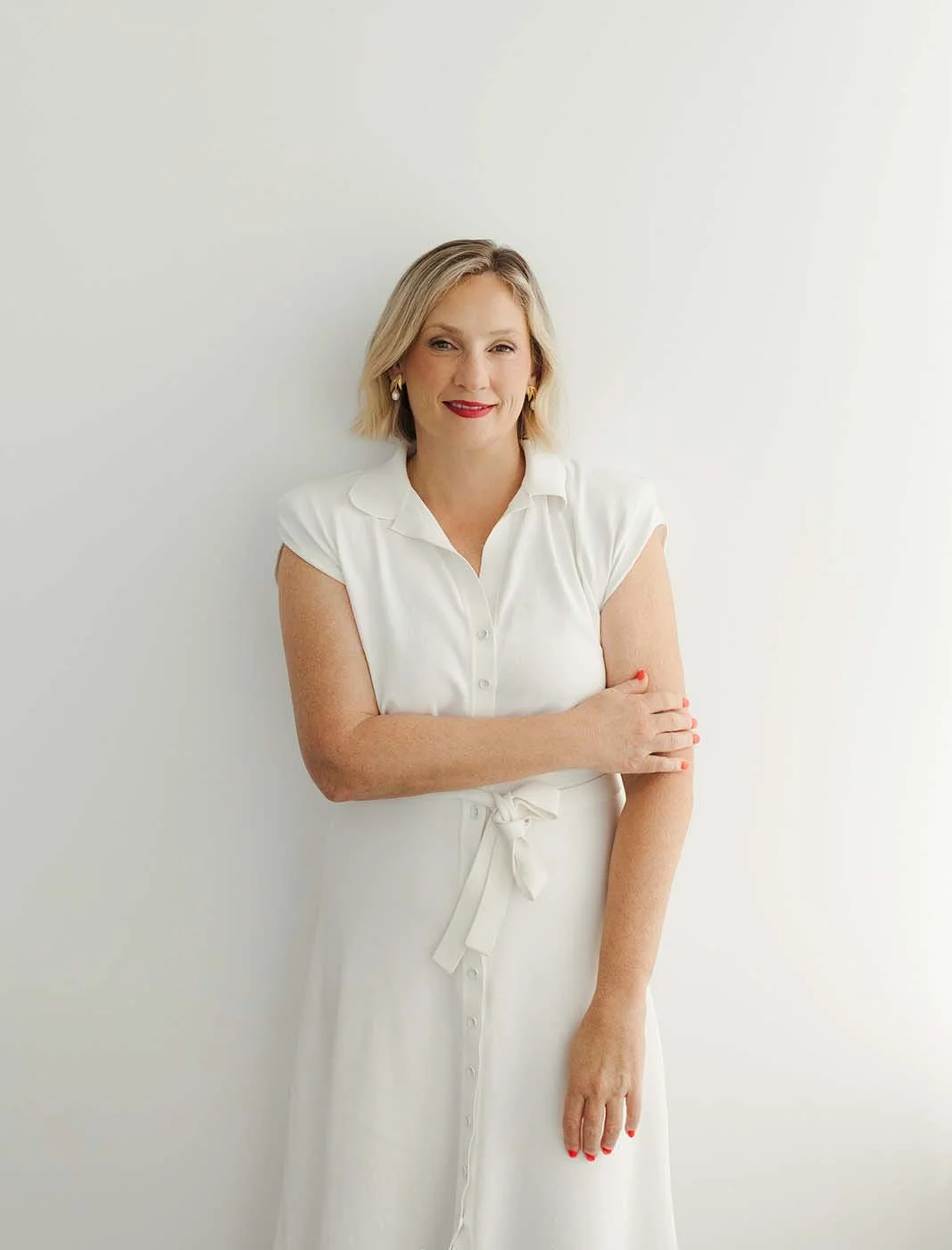 Andrea Paynter standing against a plain white background, smiling. She has with blonde hair, wearing a white dress, ready for pre-retirement planning in her Brisbane office.