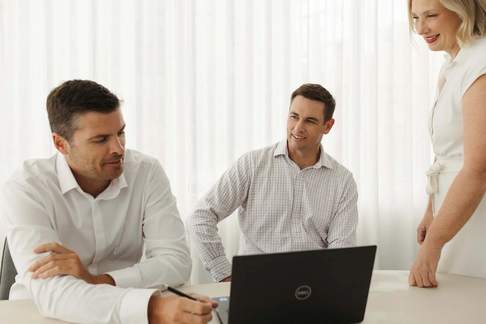 The team at Bailiwick Financial Planning - Steve Larman, David Larman and Andrea Paynter - in a business meeting in a bright office. The two men are sitting at a table with a laptop.