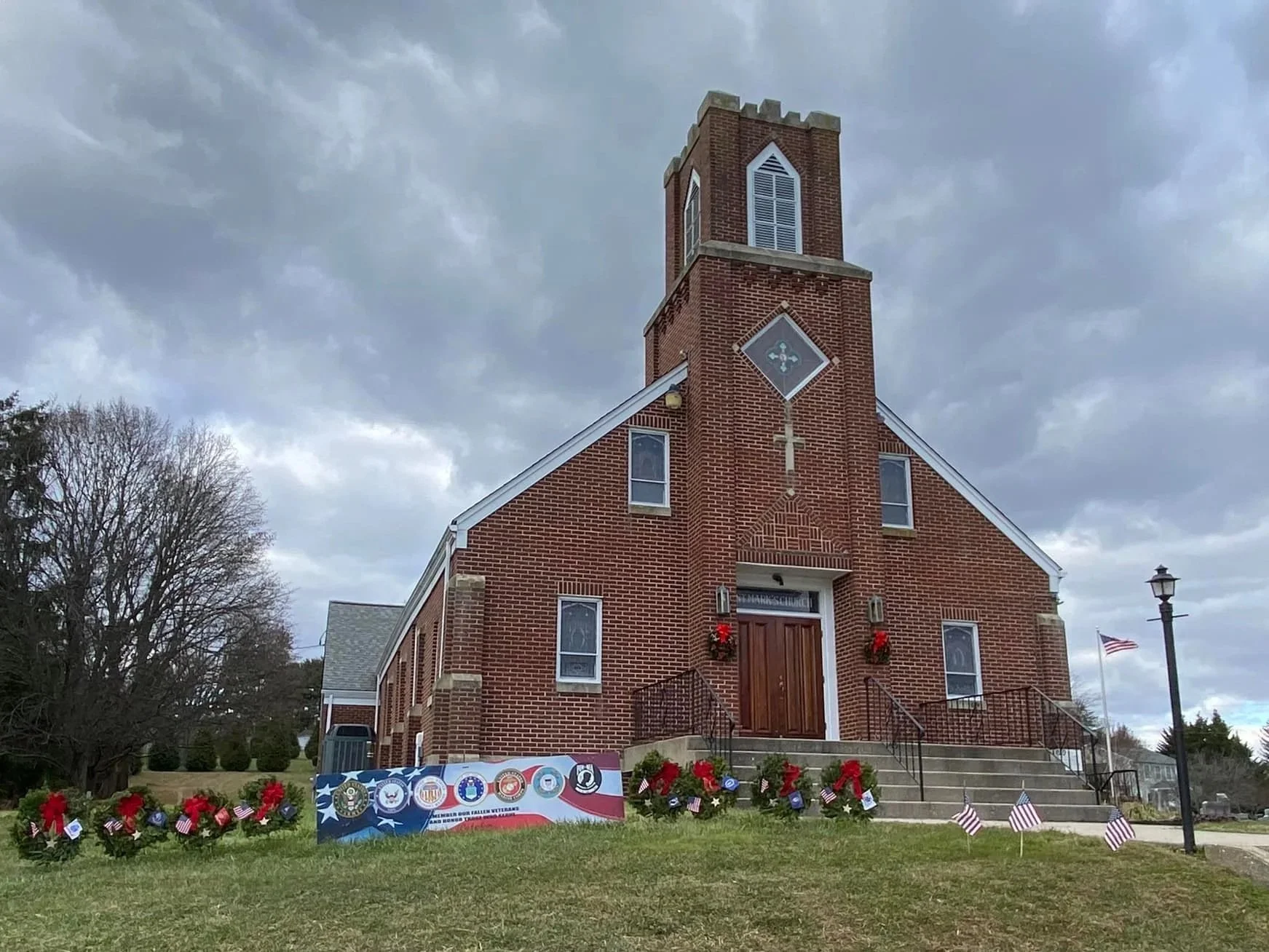A brick church decorated with red, white, and blue patriotic decorations, including American flags and wreaths, in front of a cloudy sky.