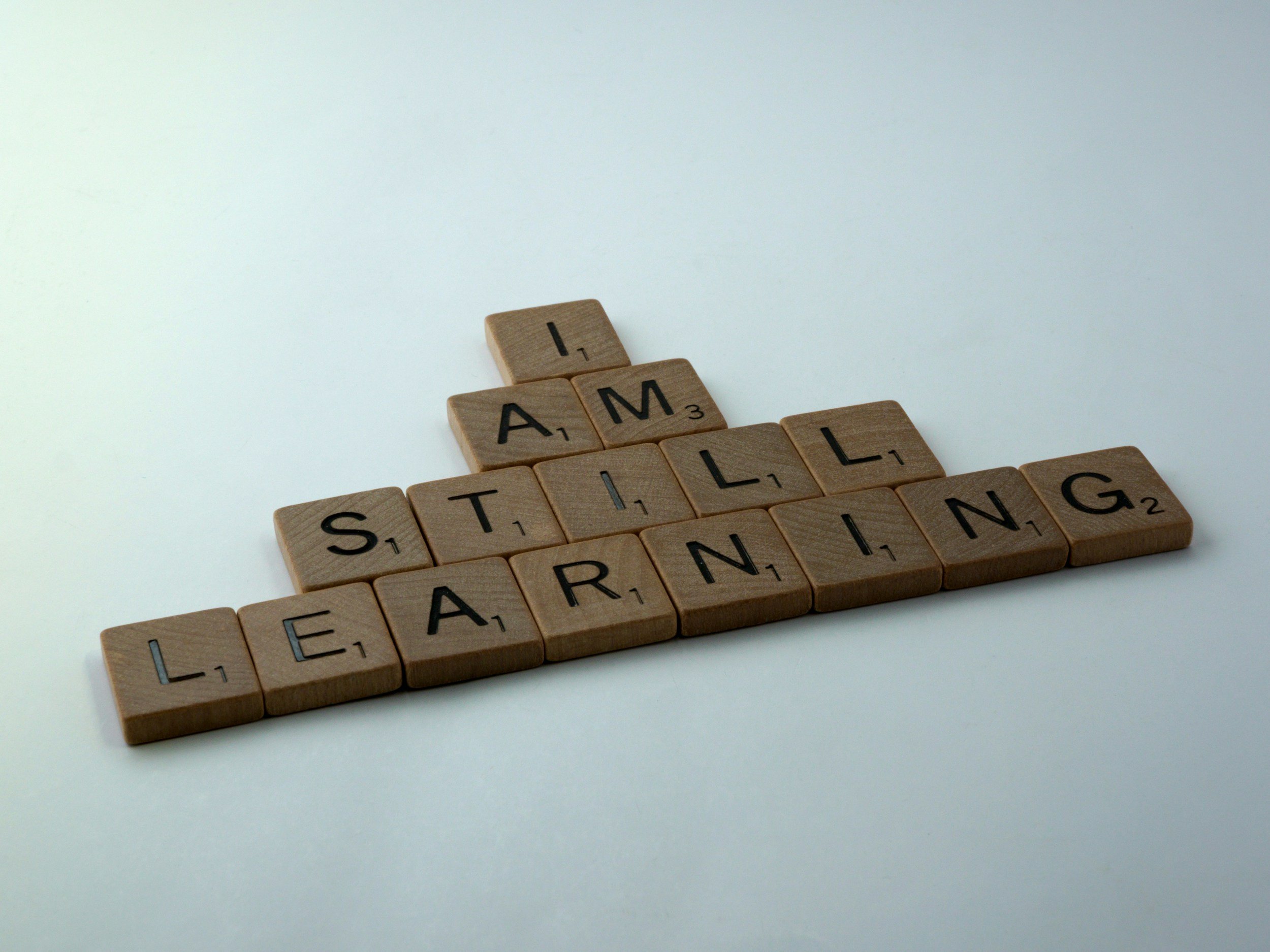 Scrabble tiles spelling out 'I AM STILL LEARNING' on a white background.