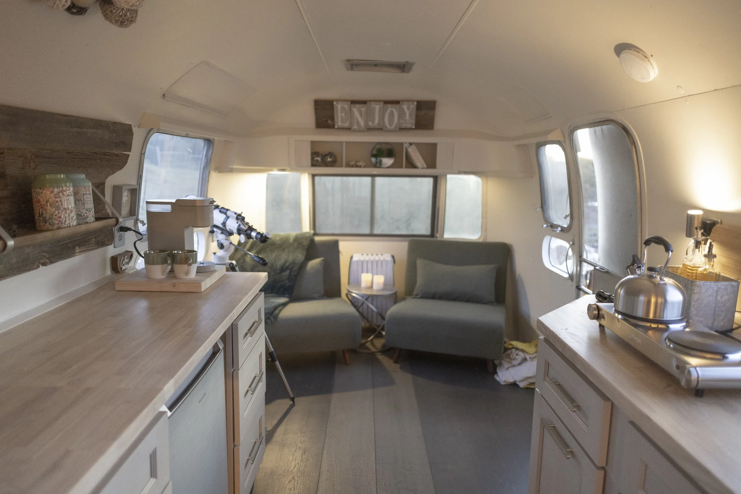 Cozy camper interior with small kitchen area, telescope, and seating area with windows and decorative items.