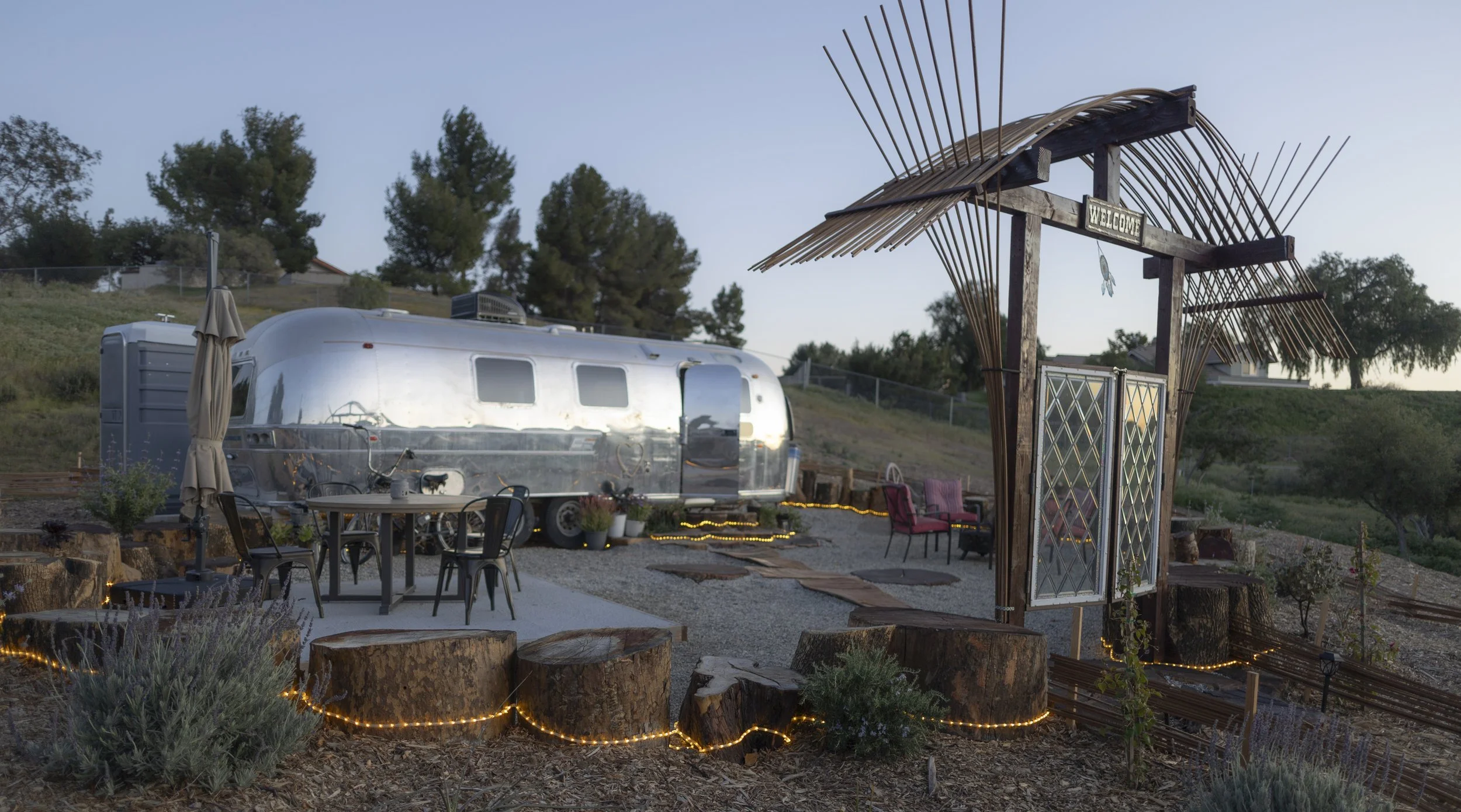 Outdoor scene featuring a vintage silver travel trailer, an entrance arch with a