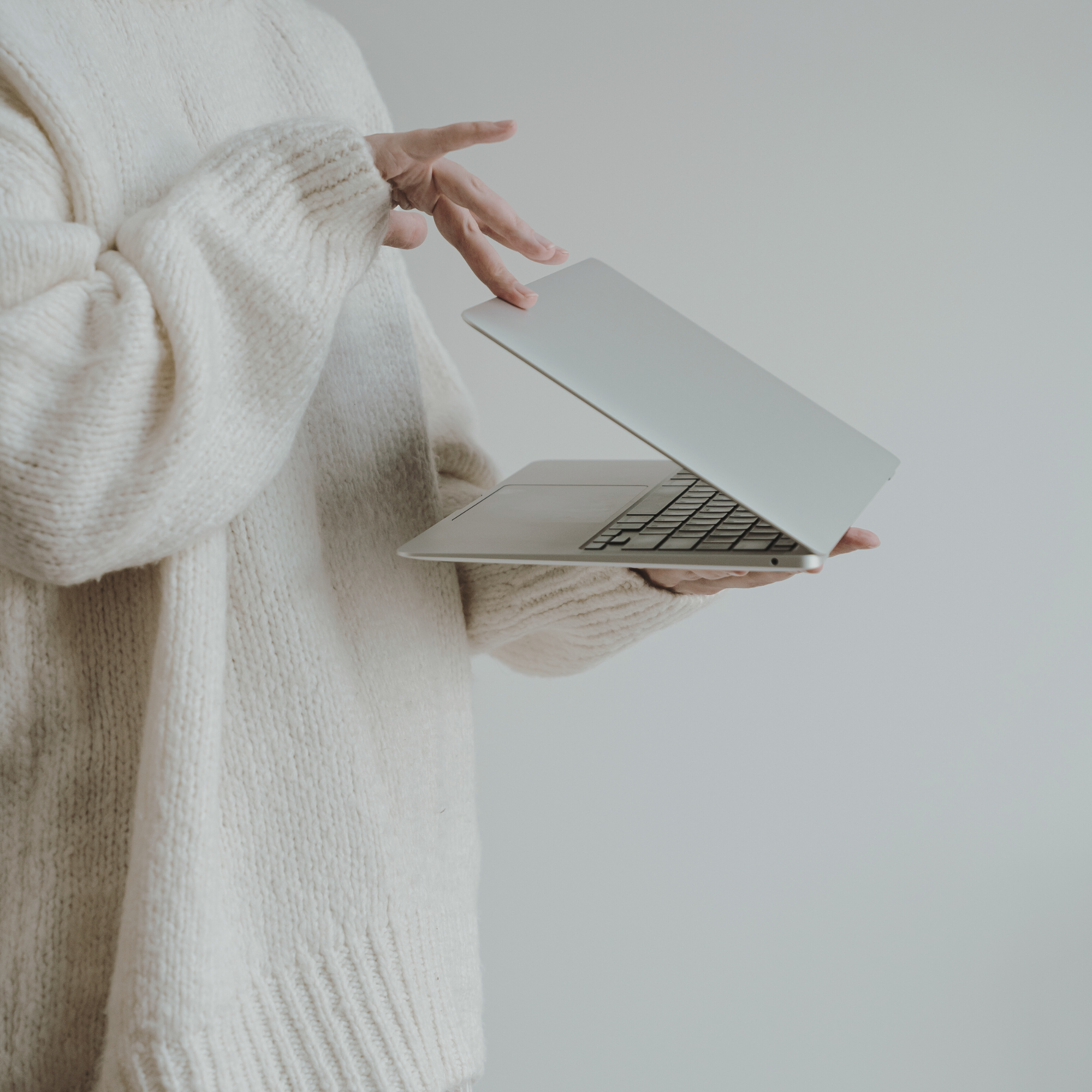 Person wearing a cream-colored knit sweater holding a silver laptop.