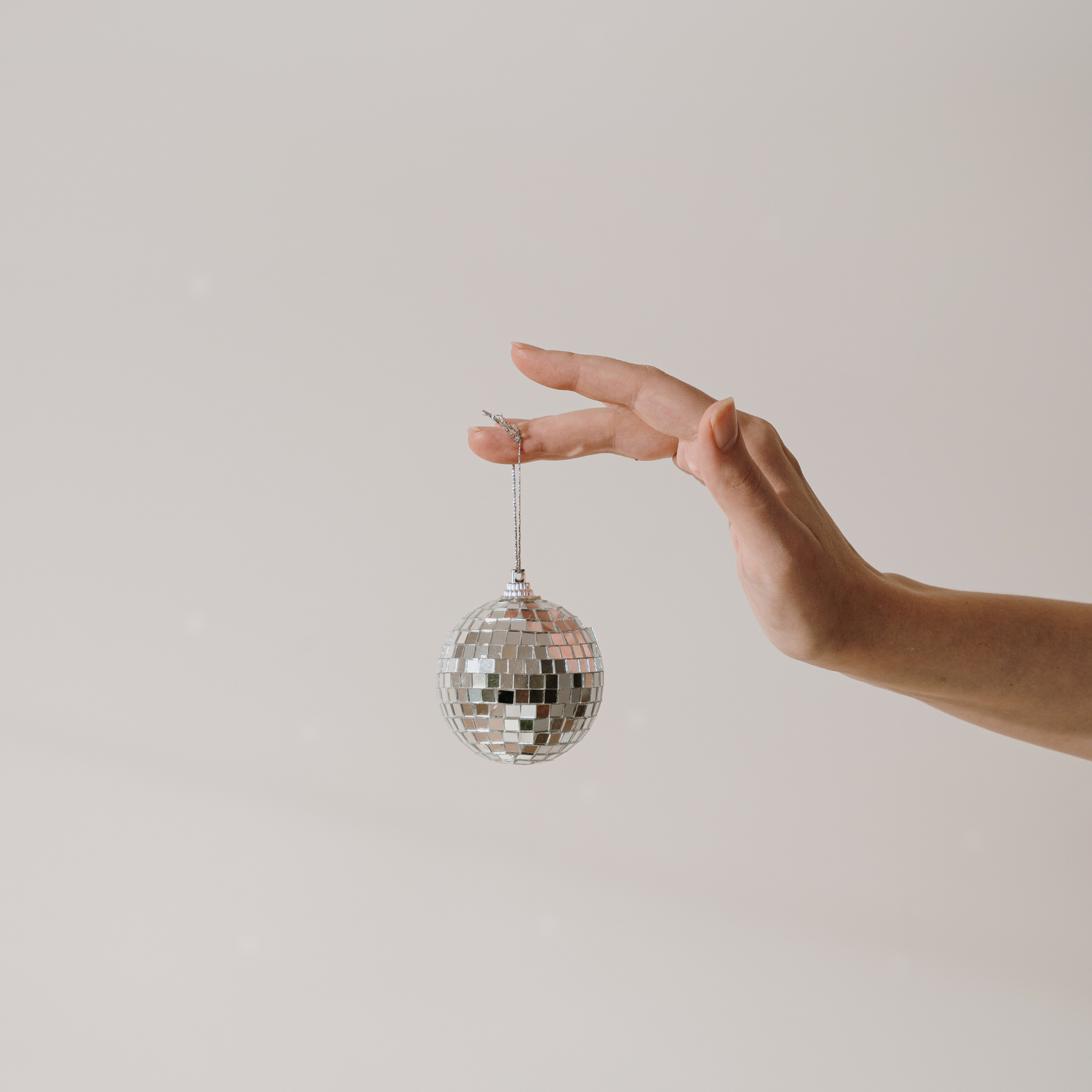 Hand holding a small disco ball ornament against a plain light background.