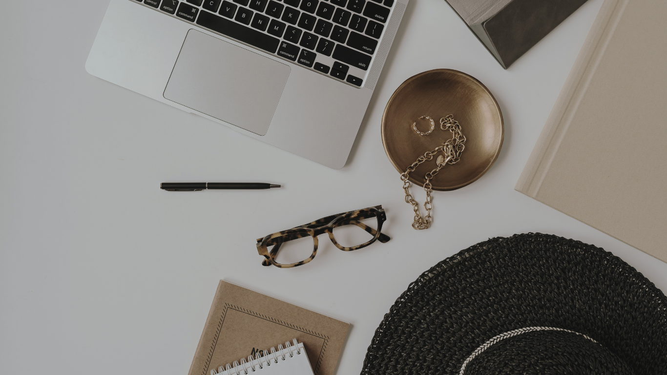 Flatlay of laptop, glasses, pens, hat, notepads and jewellery