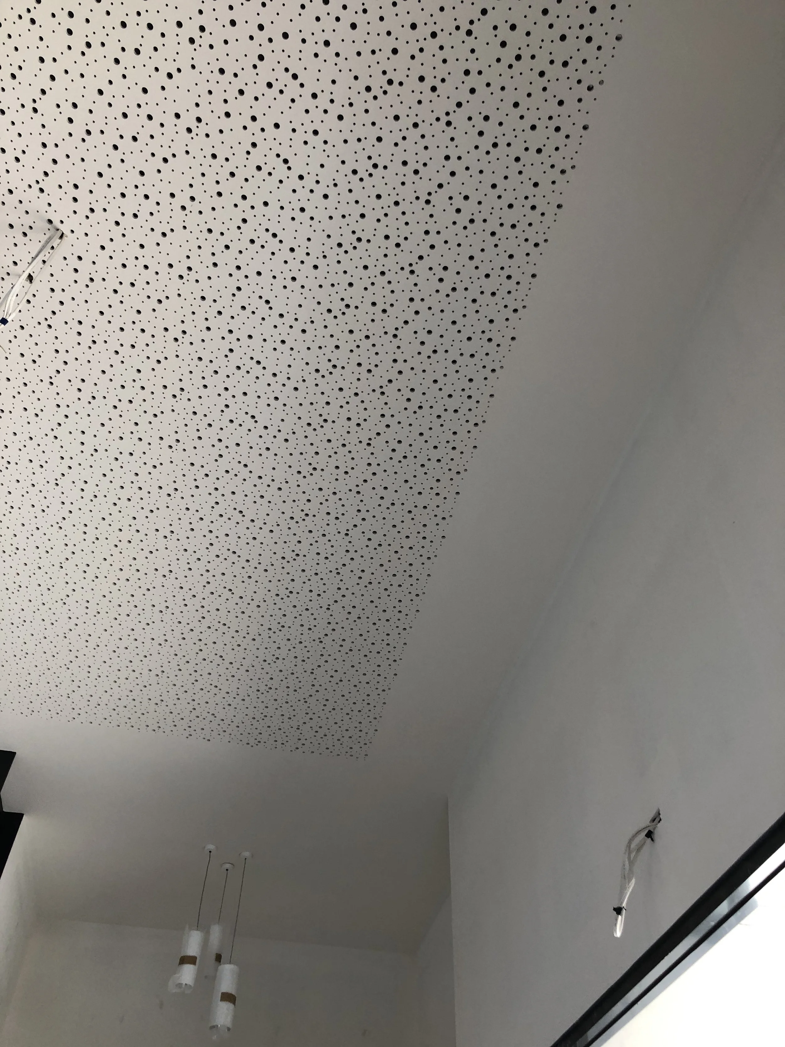 Ceiling with a perforated white acoustic panel, two hanging white pendant lights, and wires hanging from the wall.