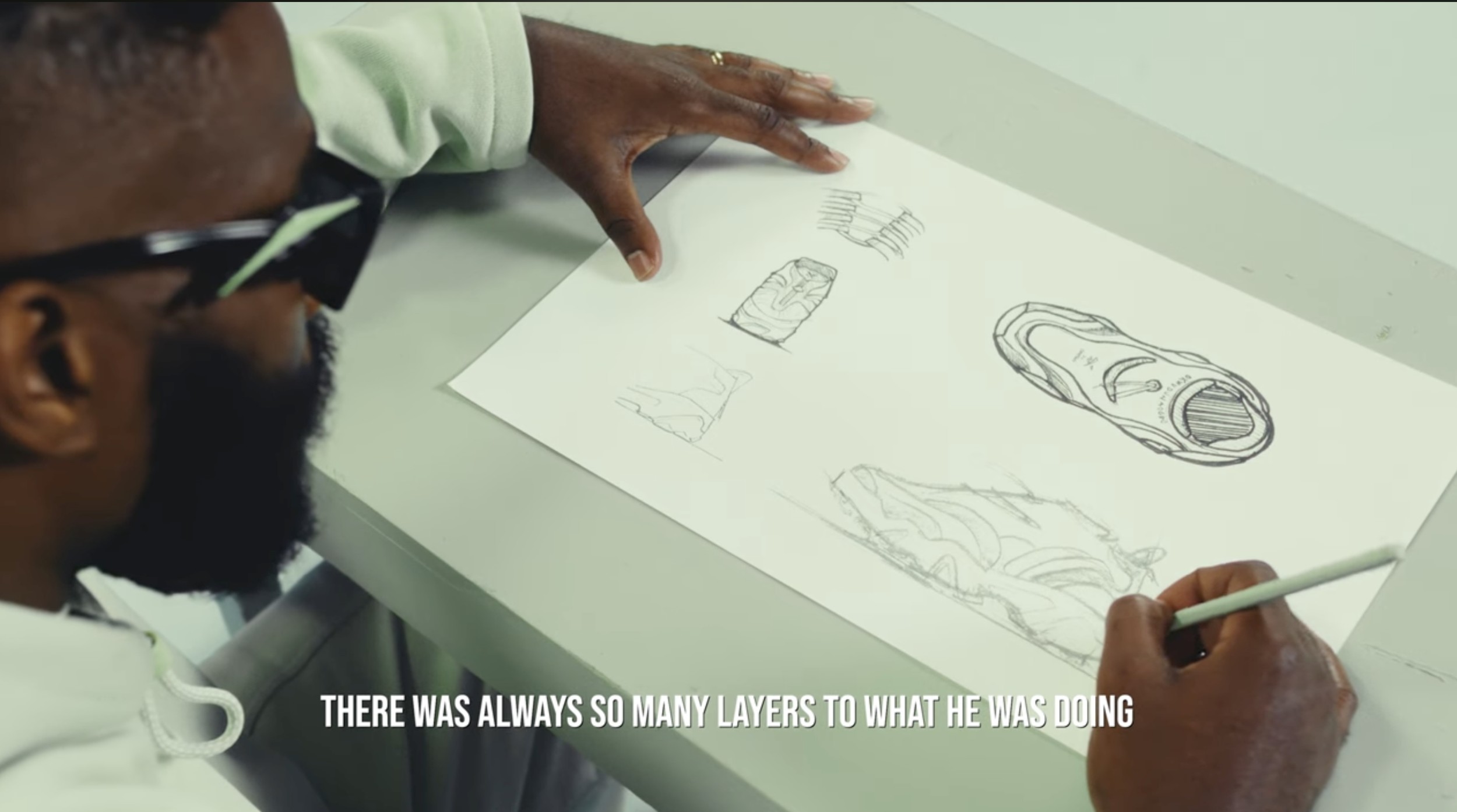 A person sketching various designs of a bottle on a large white sheet of paper, with some detailed drawings and rough sketches.