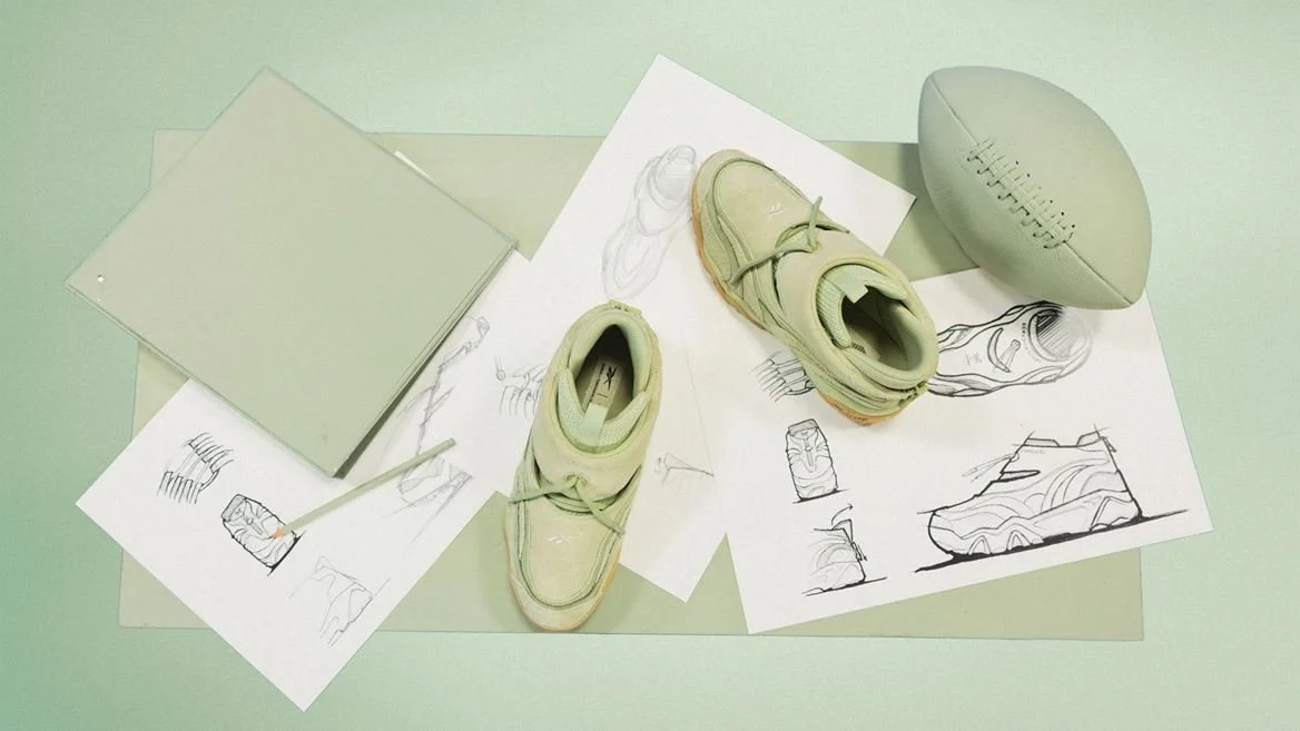 Design and sketching materials including sketches of footwear and a pair of sneakers, alongside a football with markings, set on a light-colored surface.