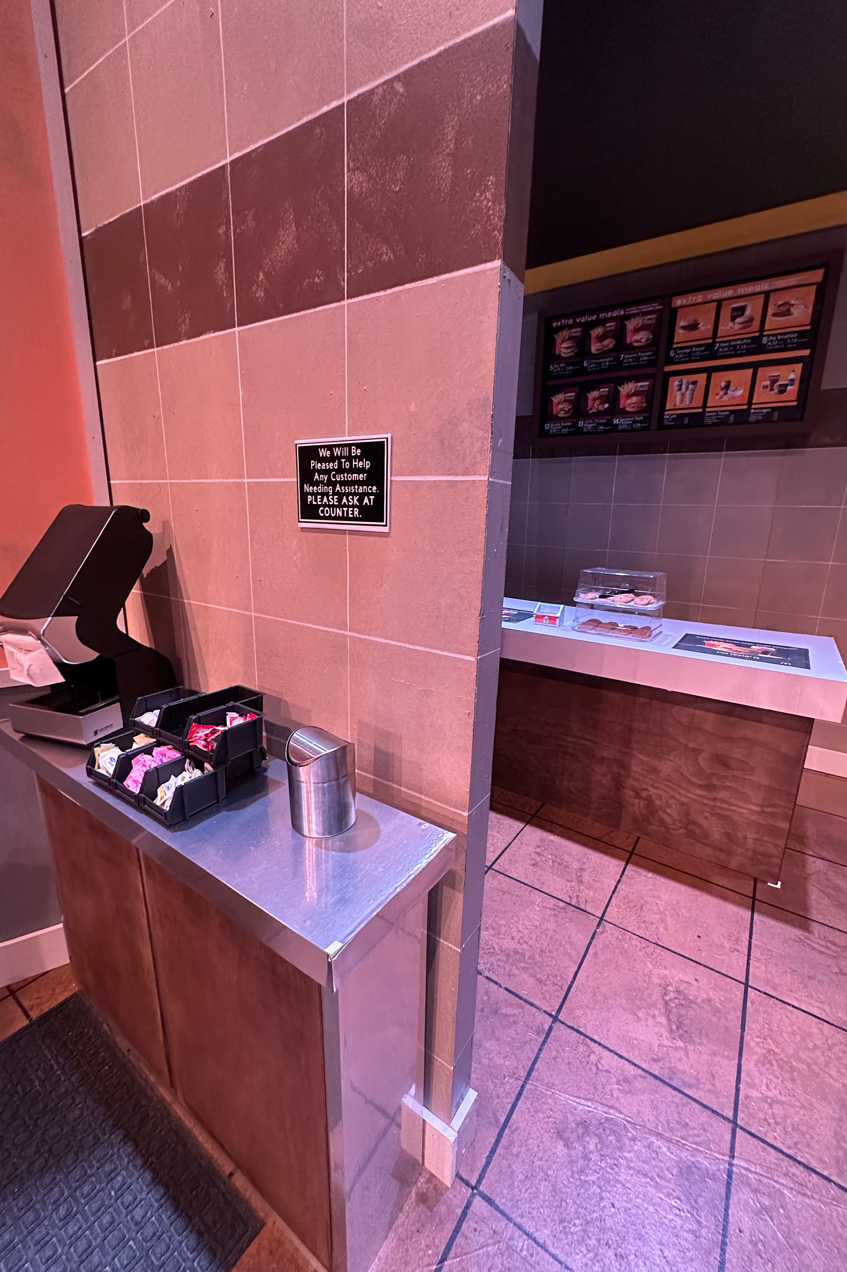 Sushi restaurant ordering area with several trays of sushi, a drink dispenser, and a sign asking customers to pay at the counter.
