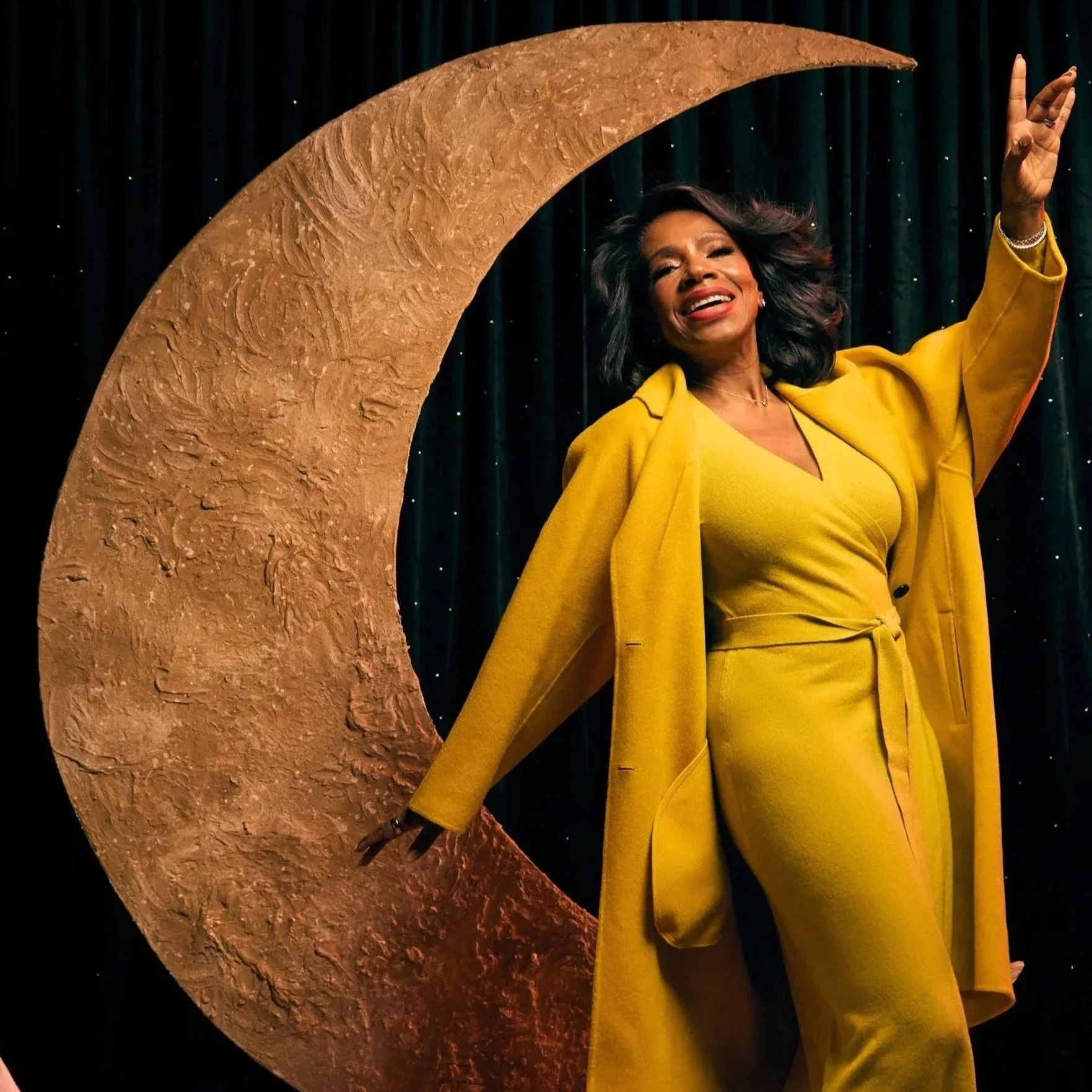 Woman in yellow outfit posing next to a large decorative crescent moon.