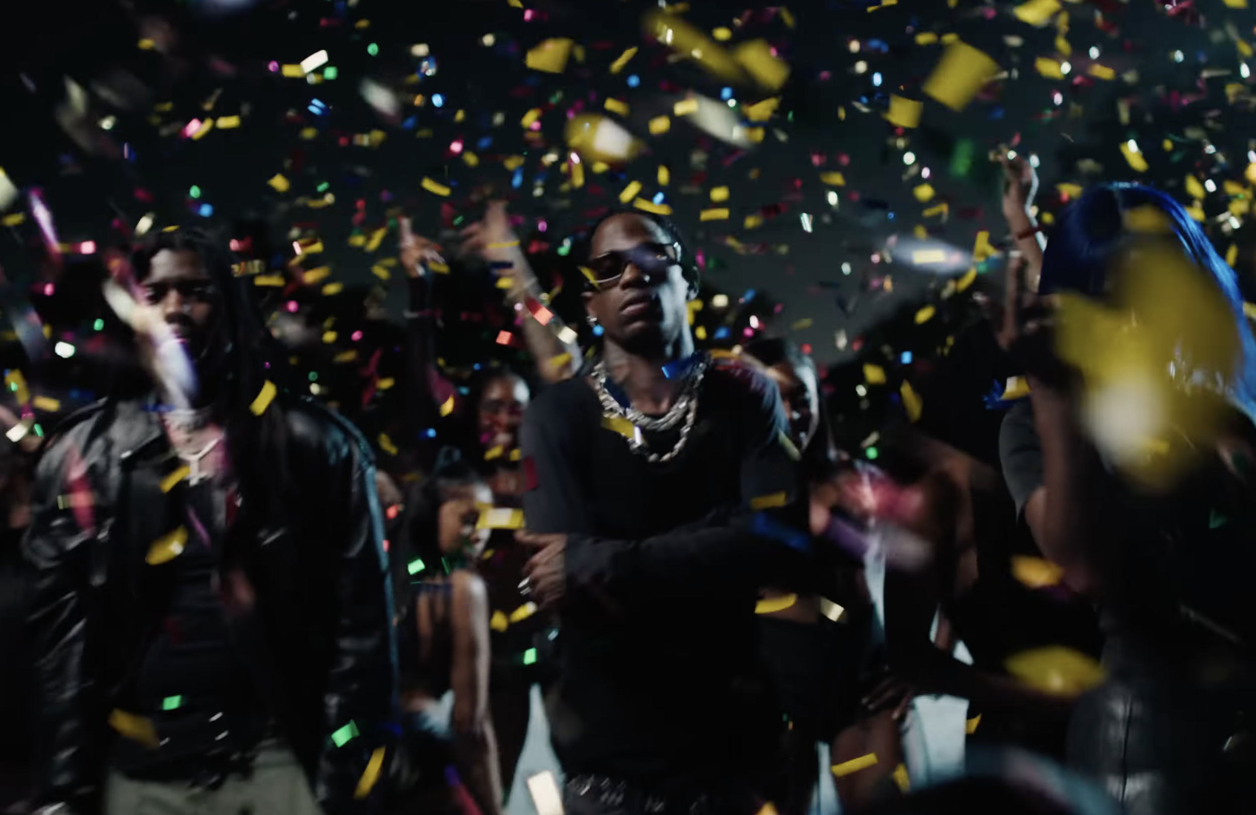 People at a party with colorful confetti falling from above, some wearing sunglasses and fashionable clothing, in a lively celebration or event.
