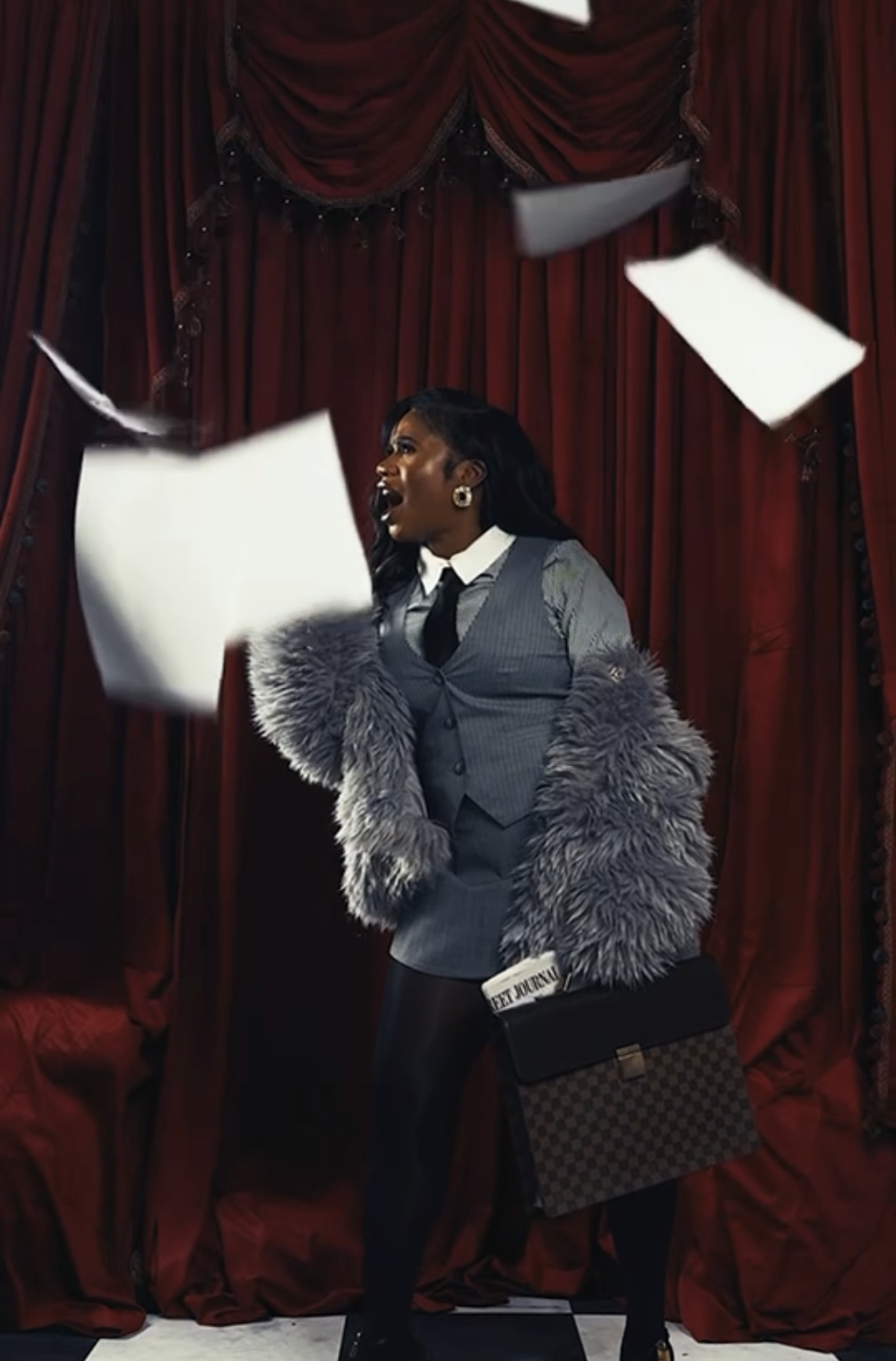 A woman standing in front of red velvet curtains, wearing a gray vest, shirt, and tie, with a faux fur coat draped over her shoulders, holding a designer bag, and shouting with papers flying around.