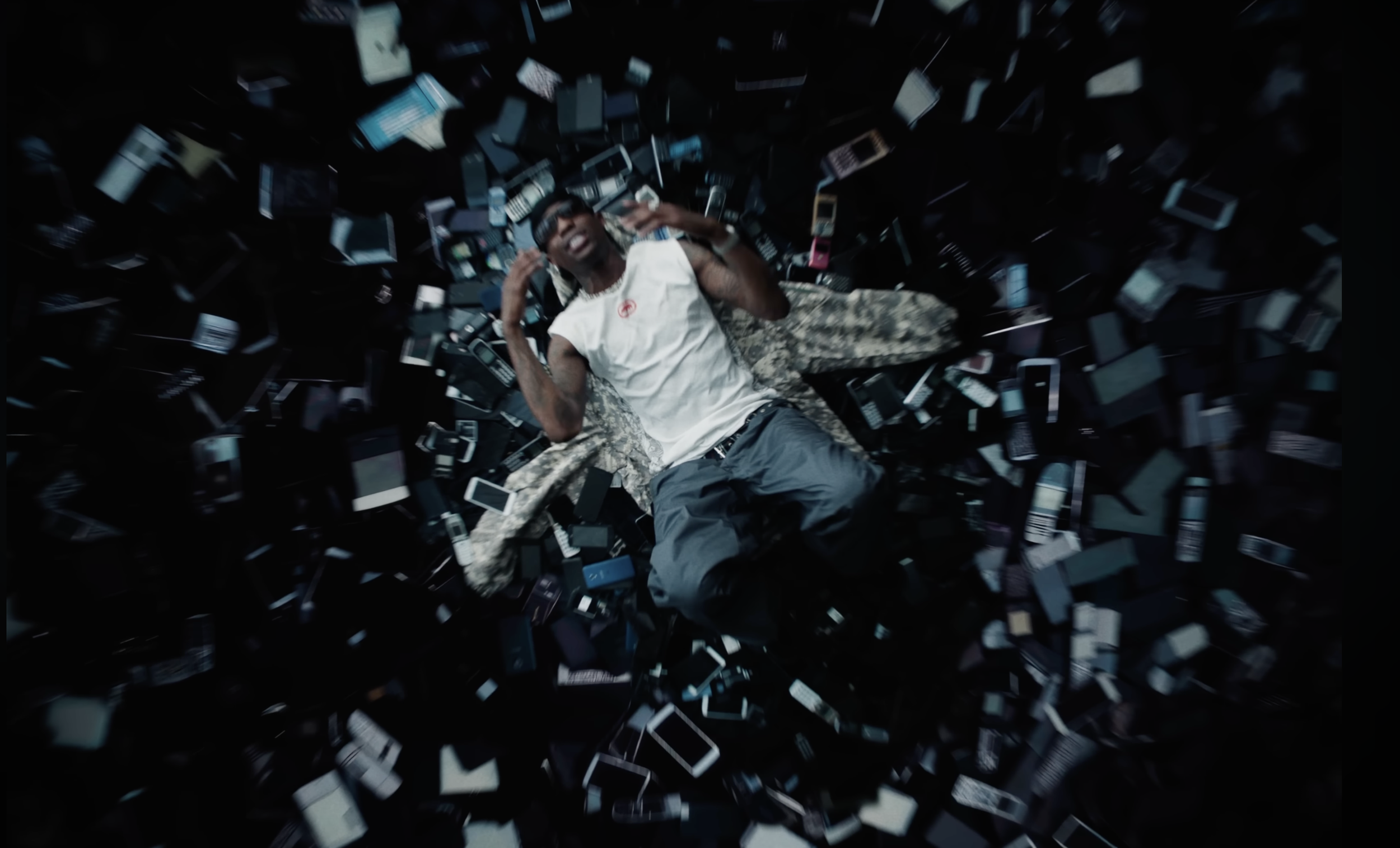 Person lying on the ground surrounded by numerous scattered mobile phones, smiling and gesturing with hands.