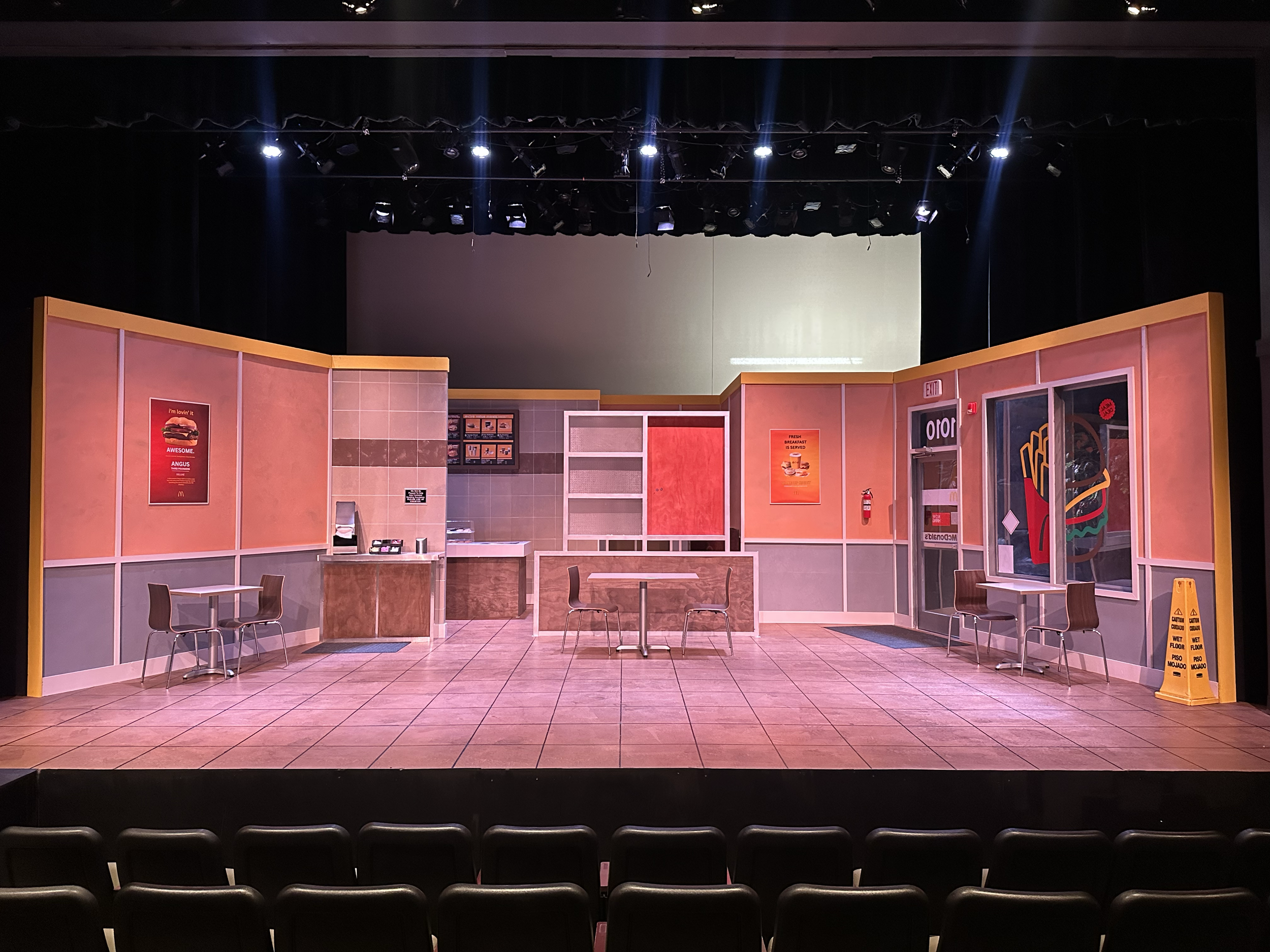A theater stage set designed to look like a fast-food restaurant with tables, chairs, and posters.