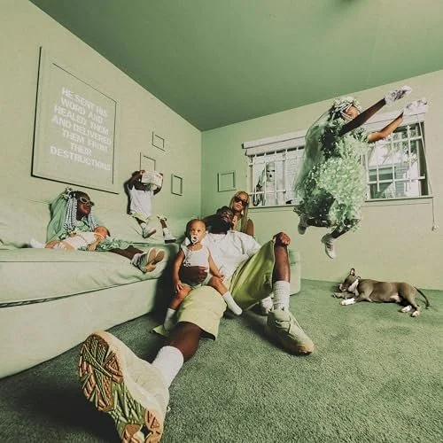 Group of children and an adult in a green room with a couch and a window, children playing on and around the couch, one jumping, a dog lying on the carpet.