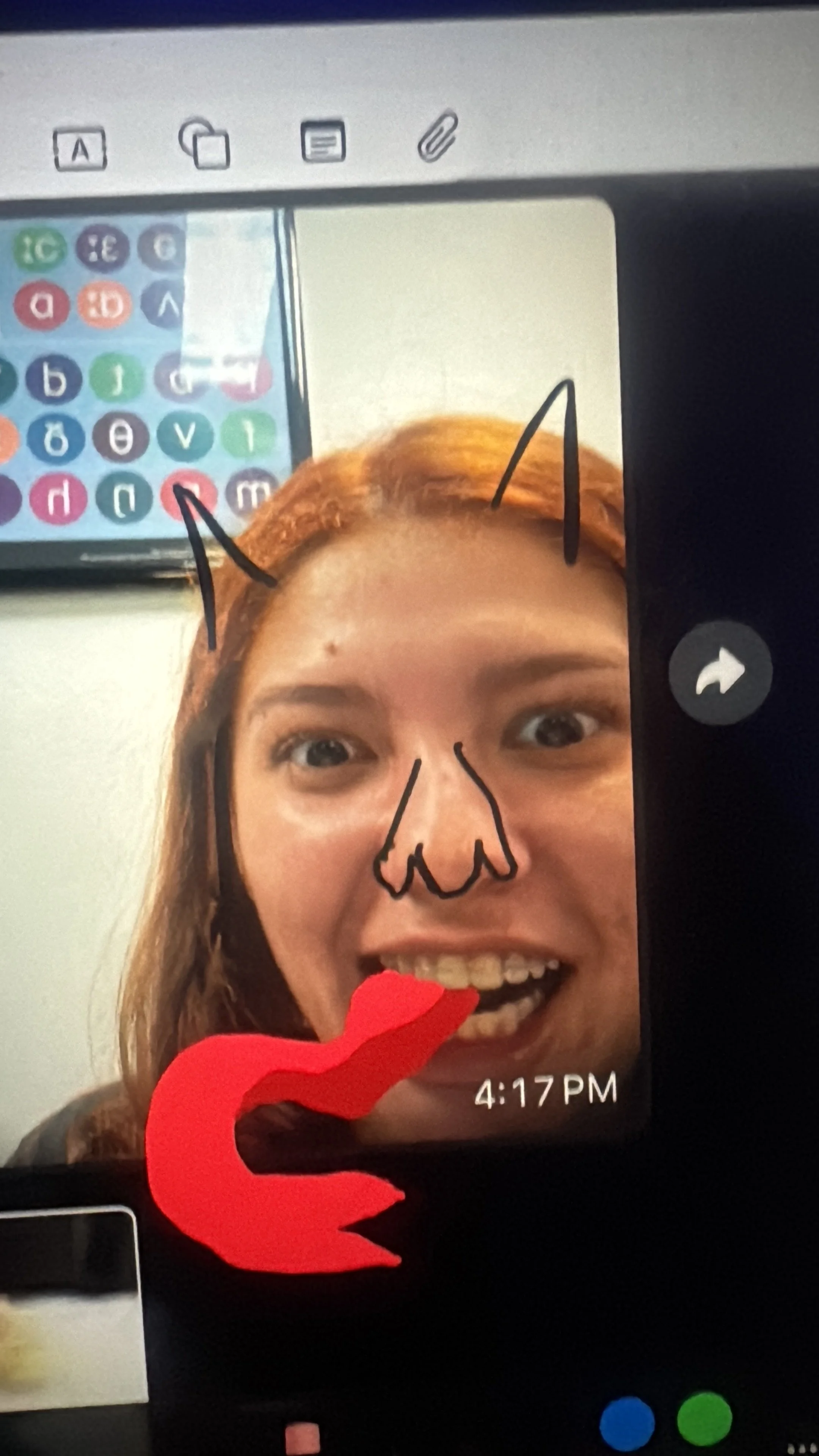 A woman taking a selfie with a digitally drawn devil horns, nose, and tail on her face. She has red hair and is smiling widely, showing her teeth.