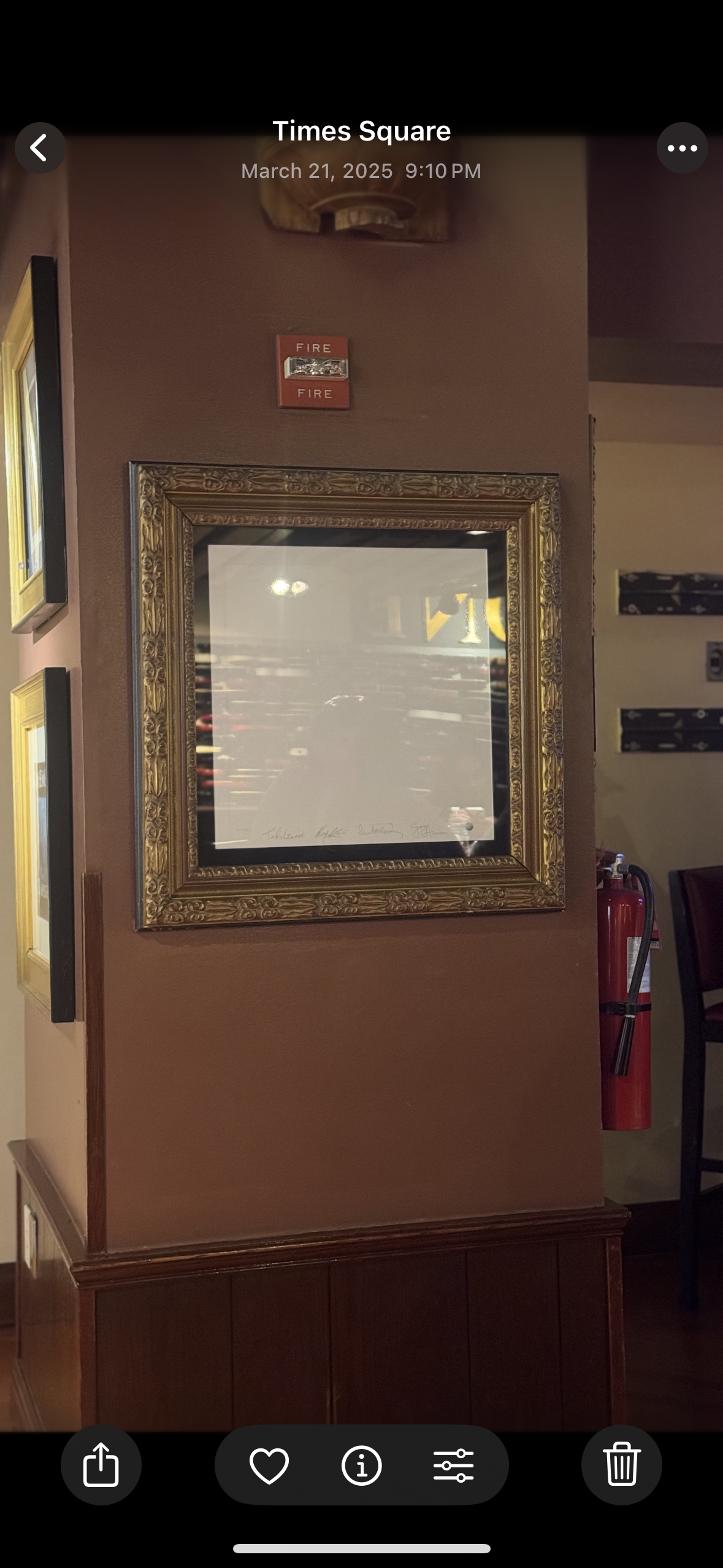 A wall with a decorative framed mirror, a red fire alarm, and a fire extinguisher. Part of a restaurant or cafe setting.