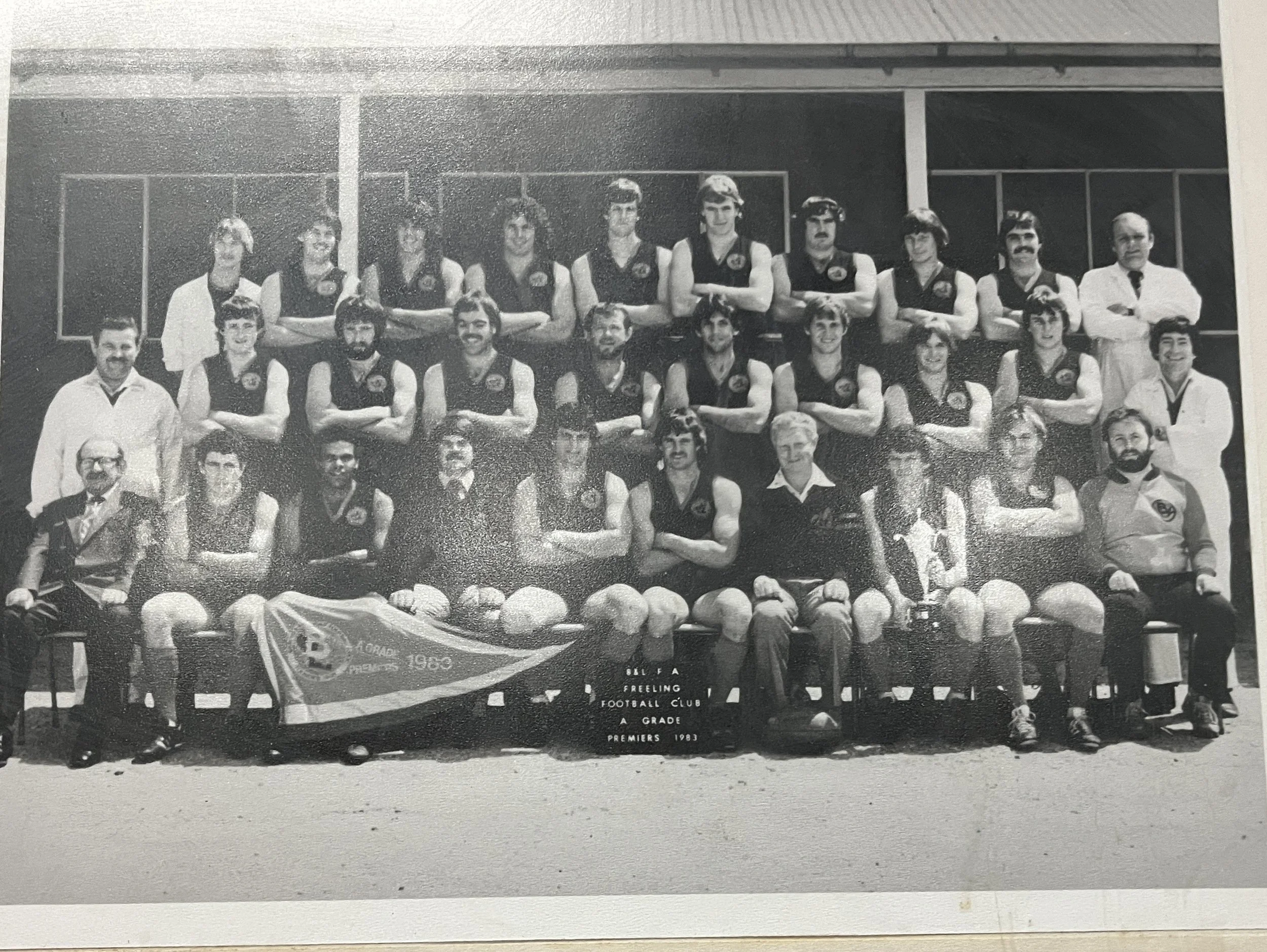 Black and white photo of a football team and staff posing for a group picture outside a building, with a banner reading 'Galfa Freeling Football Club A Grade Premiers 1983'.