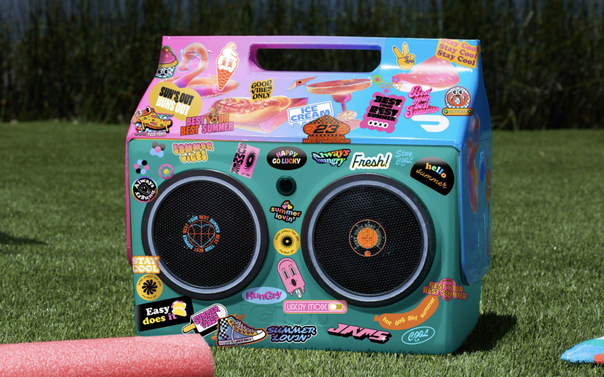 Colorful boombox decorated with stickers featuring summer-themed phrases and images, placed on grass outdoors.