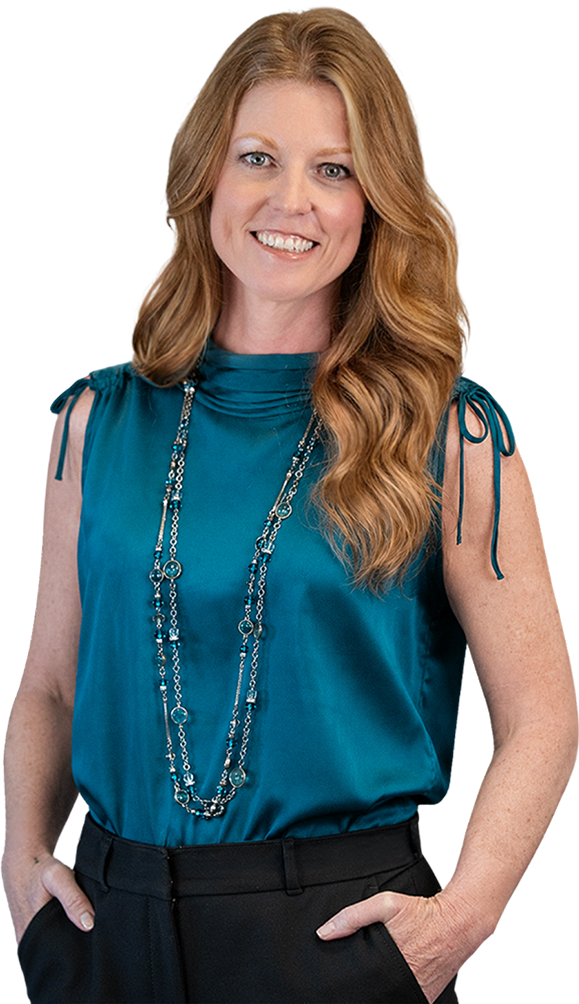 Sarah Bliss Daly, business trainer in Redding, CA wearing a teal sleeveless blouse with bow ties on the shoulders, black pants, and layered silver necklaces against a transparent background.