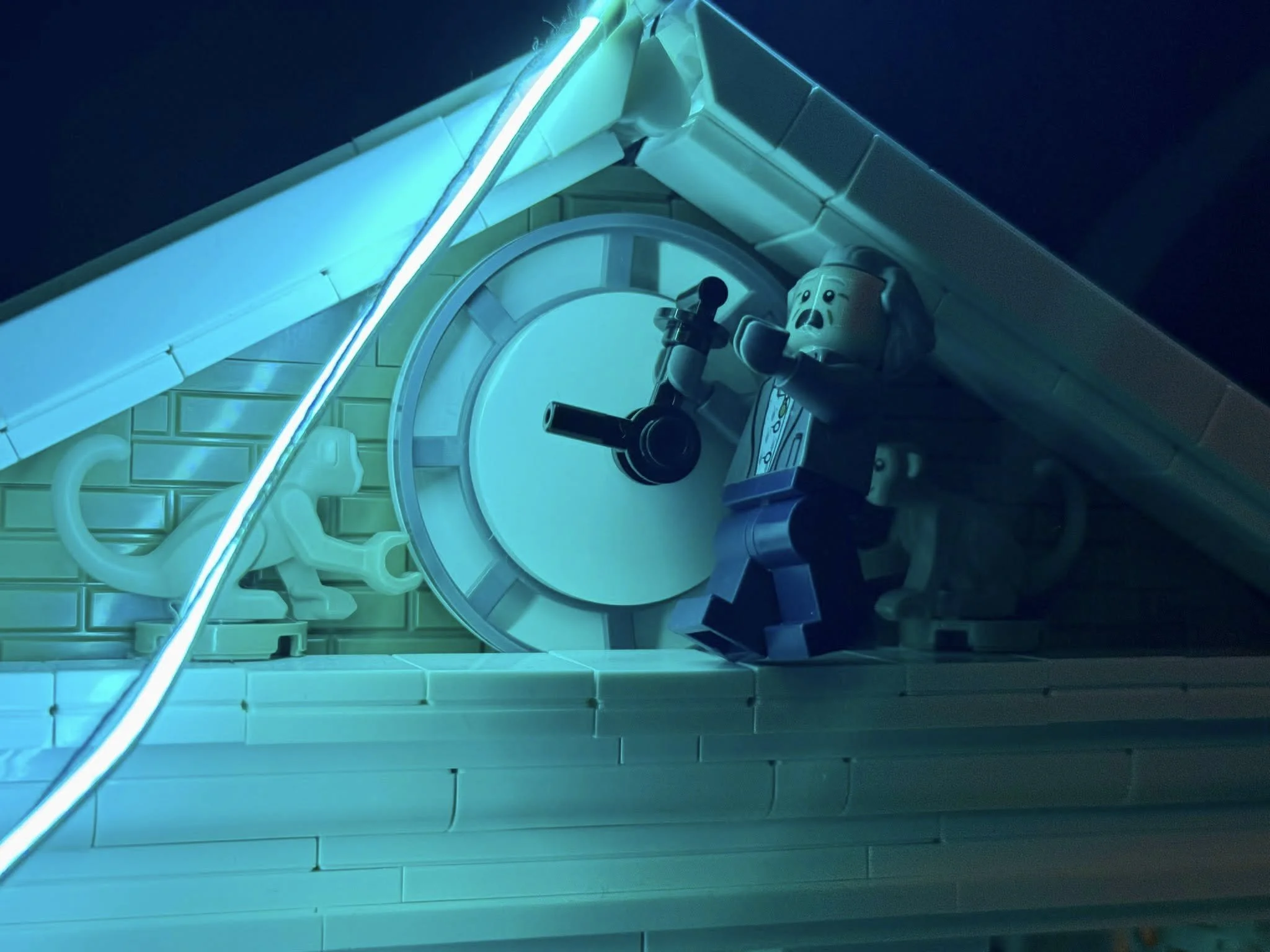 LEGO house with a sloped roof, illuminated by blue neon, featuring a clock, a LEGO man holding a cup, and a small LEGO dog statue inside.