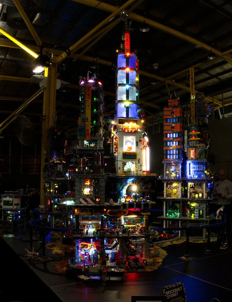 Nighttime display of a large LEGO cityscape with illuminated buildings, roads, and structures, resembling a modern city skyline.