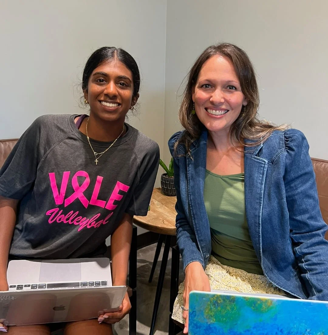 Two women smiling and sitting with laptops at a table prepping for college success together.