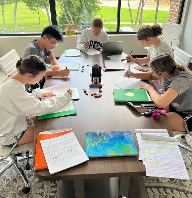 Five students sit around a table, focused on college prep, working on papers and laptops with binders and notebooks open.