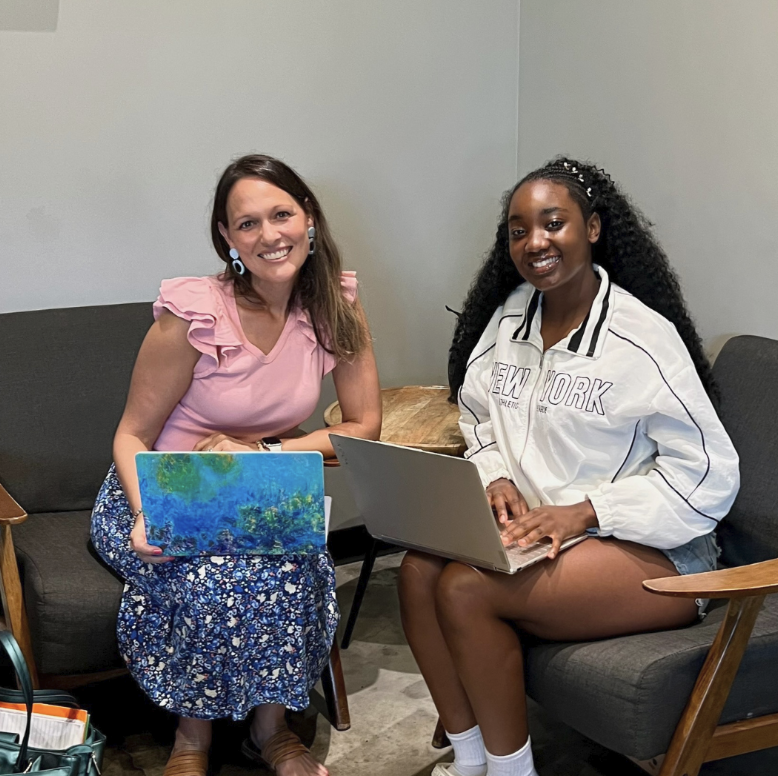 Two women sitting on chairs with laptops, smiling at the camera, discussing college prep in a casual indoor setting.