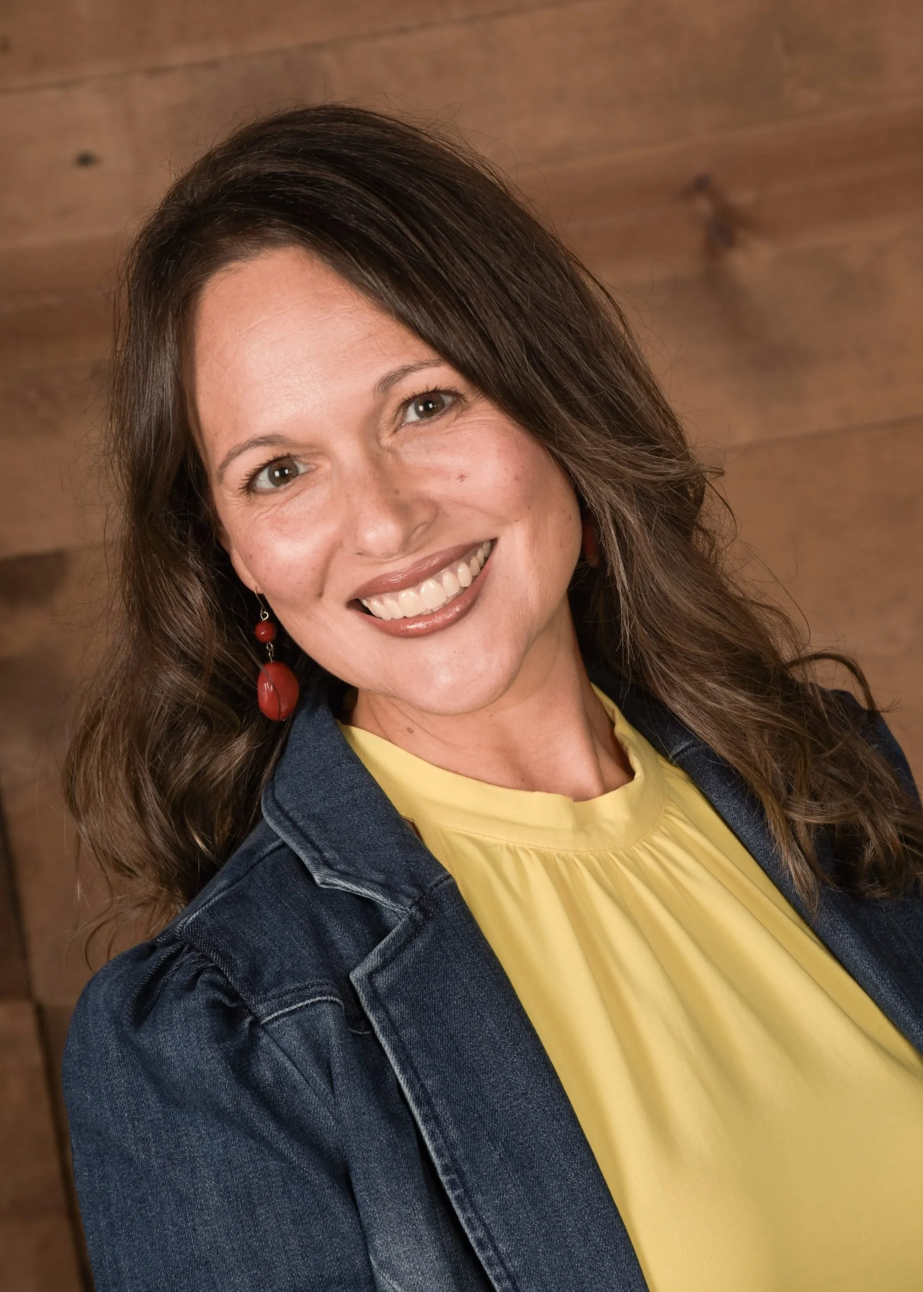 Angela Henderson Smith smiles in a yellow top and denim jacket, ready for college prep, standing by a wooden background.