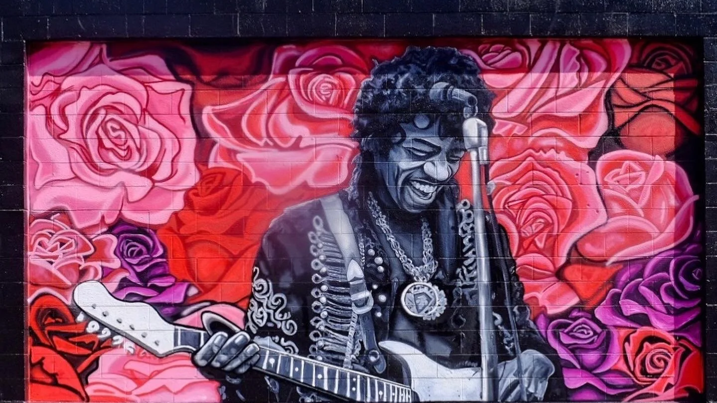 Graffiti mural of a man playing an electric guitar, smiling, surrounded by pink and purple roses.