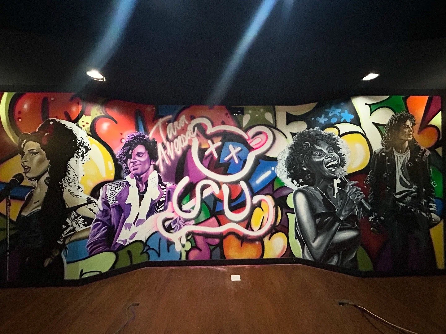 Colorful wall mural featuring portraits of women singers and graffiti-style art, with vibrant abstract shapes and neon highlights.