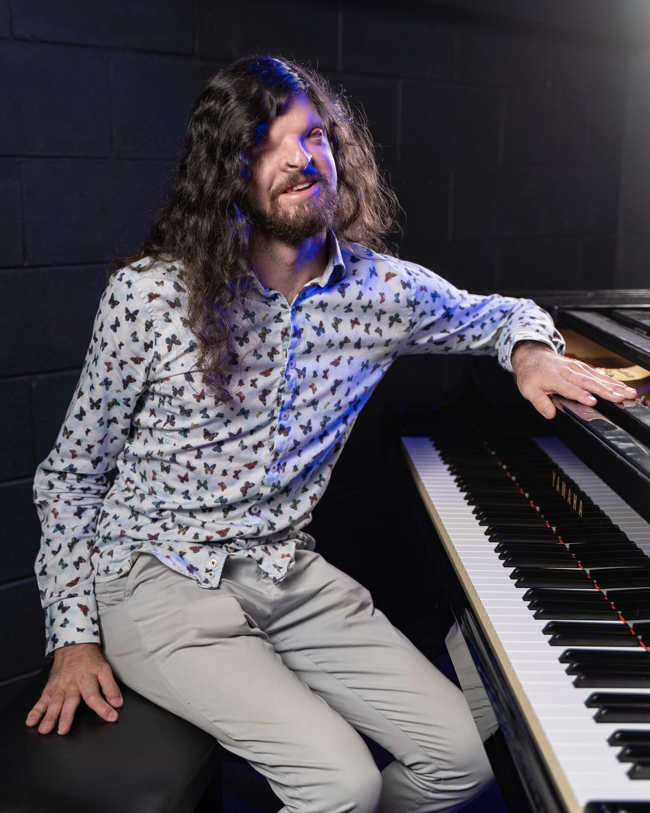 Richard sitting perpendicular to the piano with his arm across the open lid