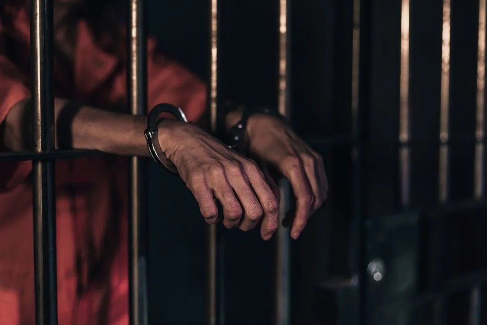 image from rawpixel.com person in handcuffs, body behind bars, hands through the cell bars