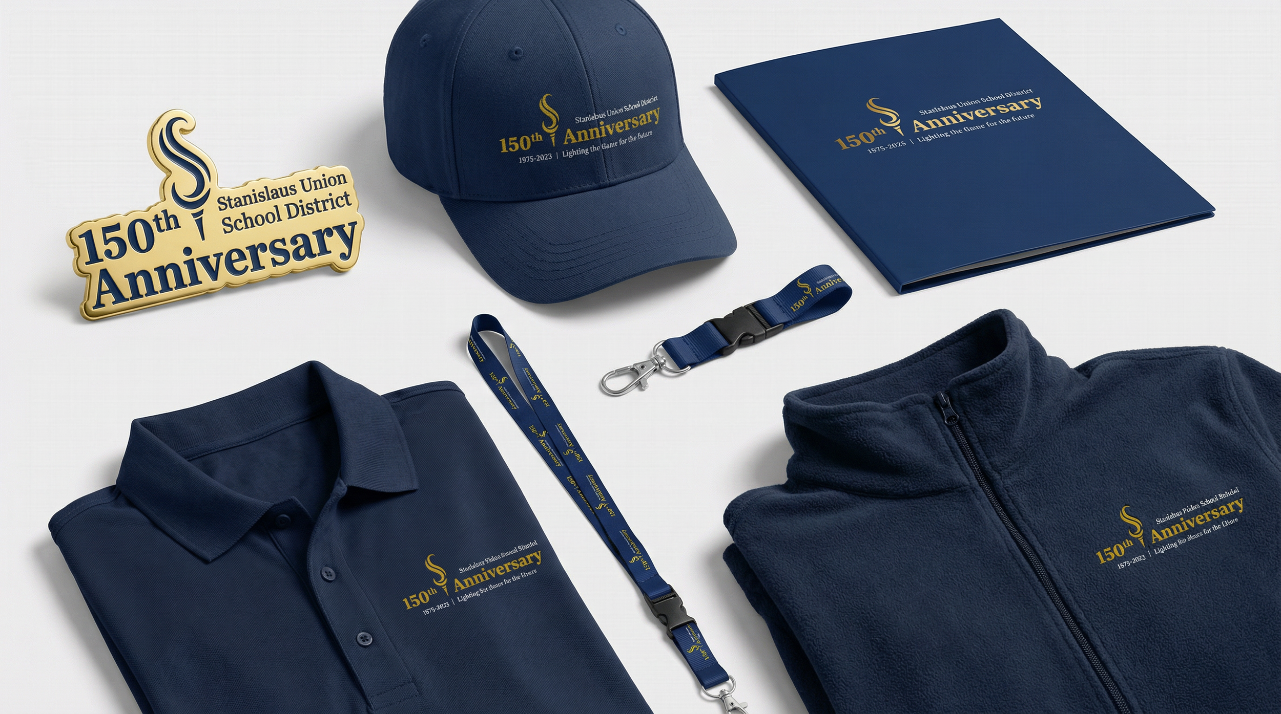 Items celebrating the 150th anniversary of Stanislaus Union School District, including a badge, hat, notebook, polo shirt, fleece jacket, and lanyard, all in blue with gold and white text.