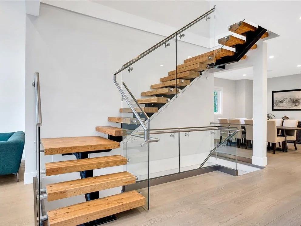 Modern wooden staircase with glass and metal railing in a bright, open home interior.
