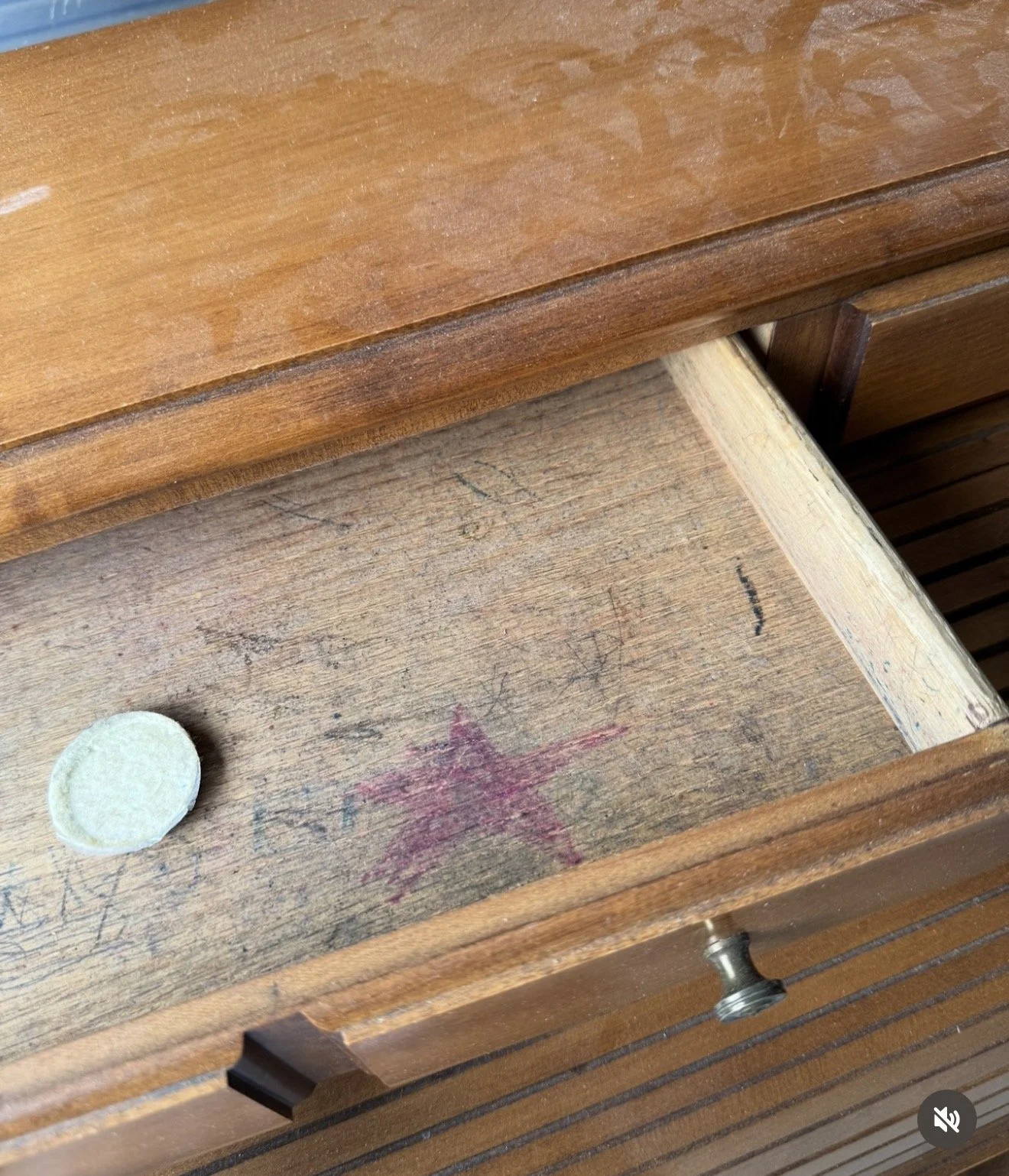 Open wooden drawer with a red star (possibly painted or drawn) on the bottom surface and a white circular object inside.