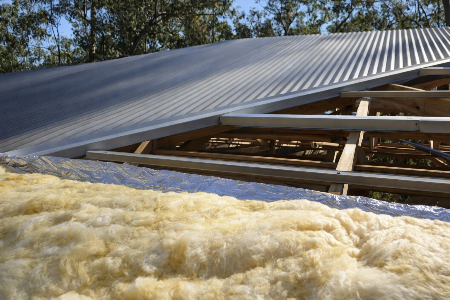 Construction site with a partially built wooden structure, metal roofing, and spray foam insulation in the foreground.