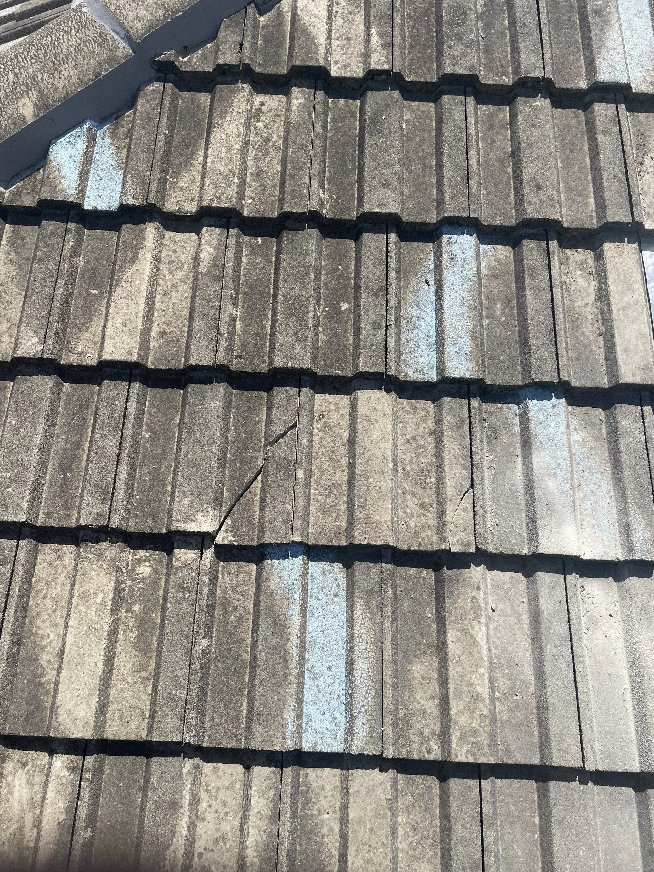 Close-up of roof shingles with some blue paint marks and cracks.