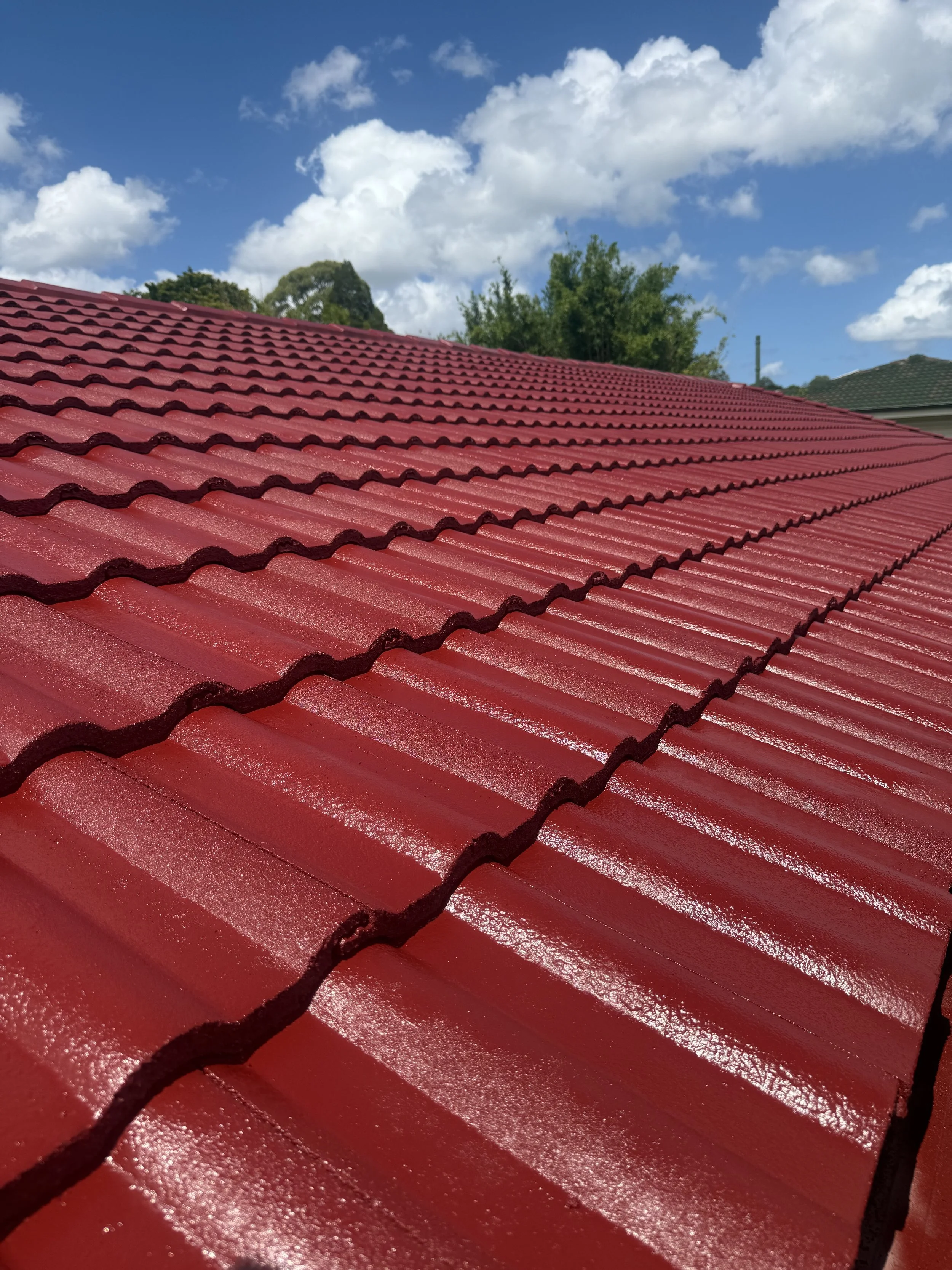 Close-up of a red, tiled roof with a background of sky and trees.