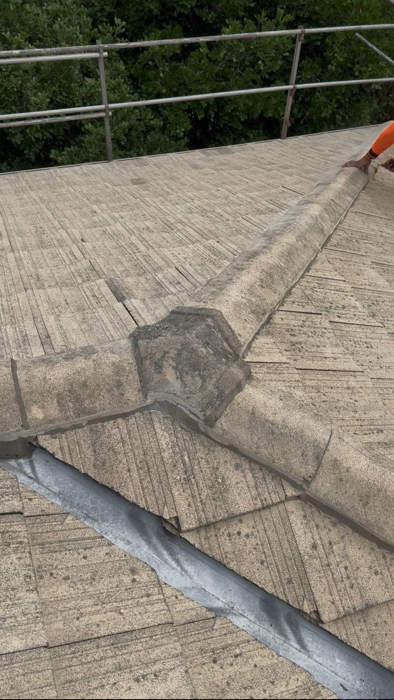 Close-up of a roof with a person in an orange sleeve inspecting the shingles.