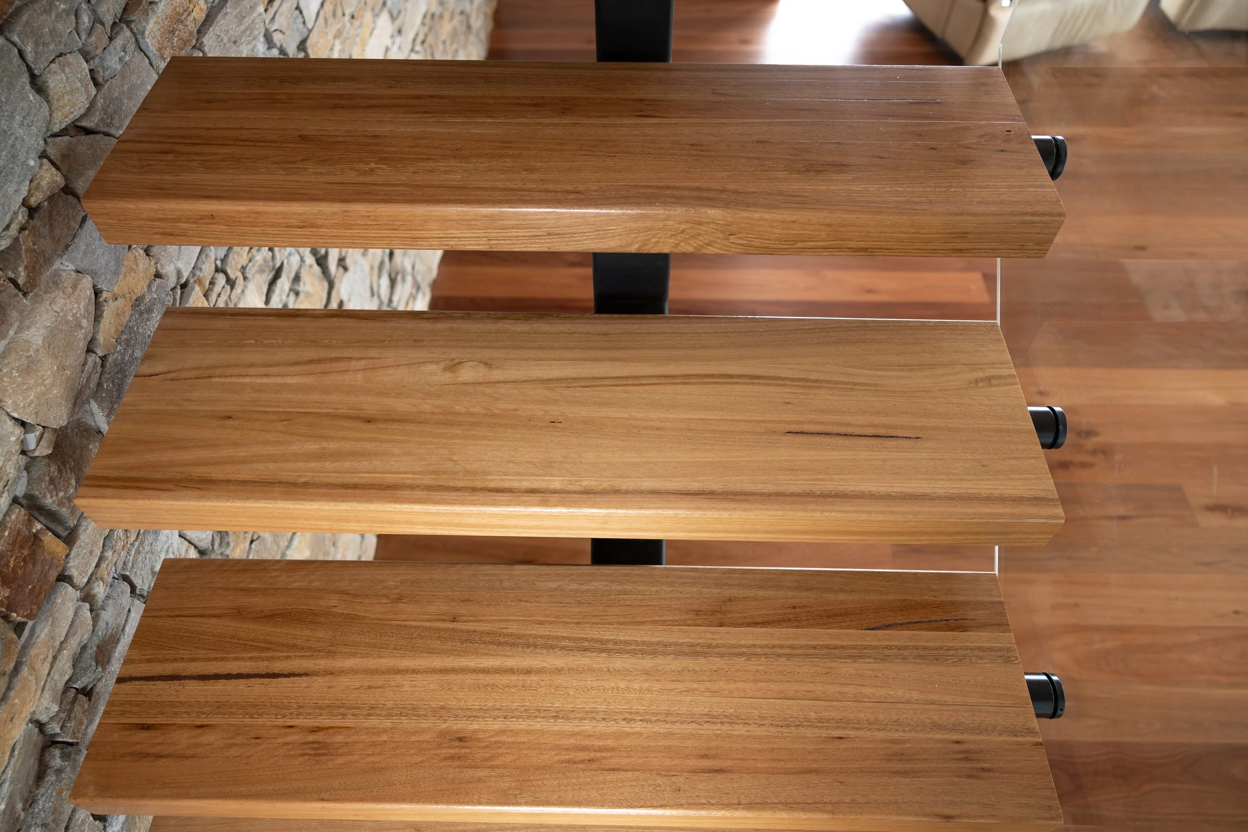Three blackbutt wooden stairs with a stone wall on the left and a wooden floor in the background.