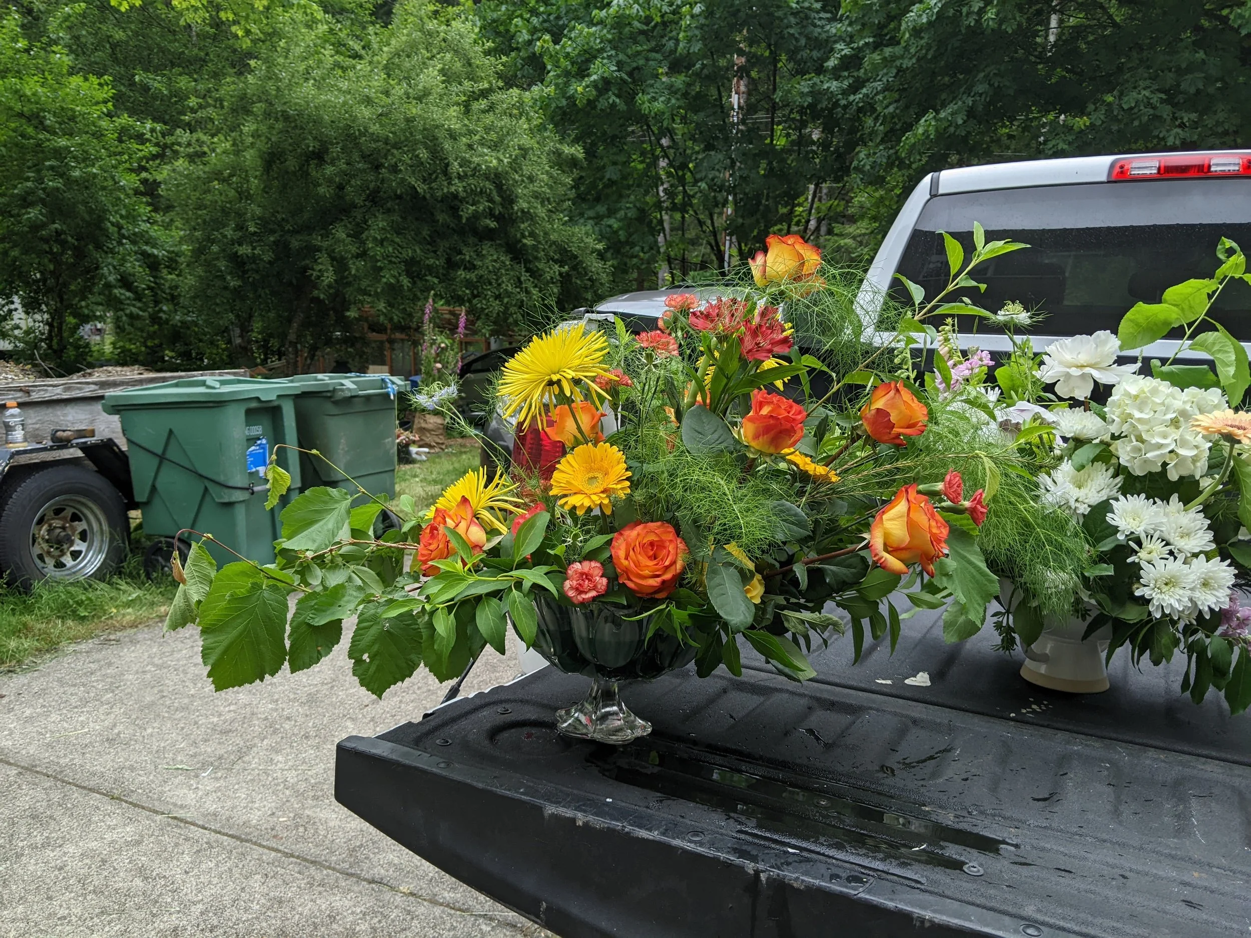 Bouquet of colorful flowers including roses, daisies, and other blooms on the tailgate of a truck in a driveway.