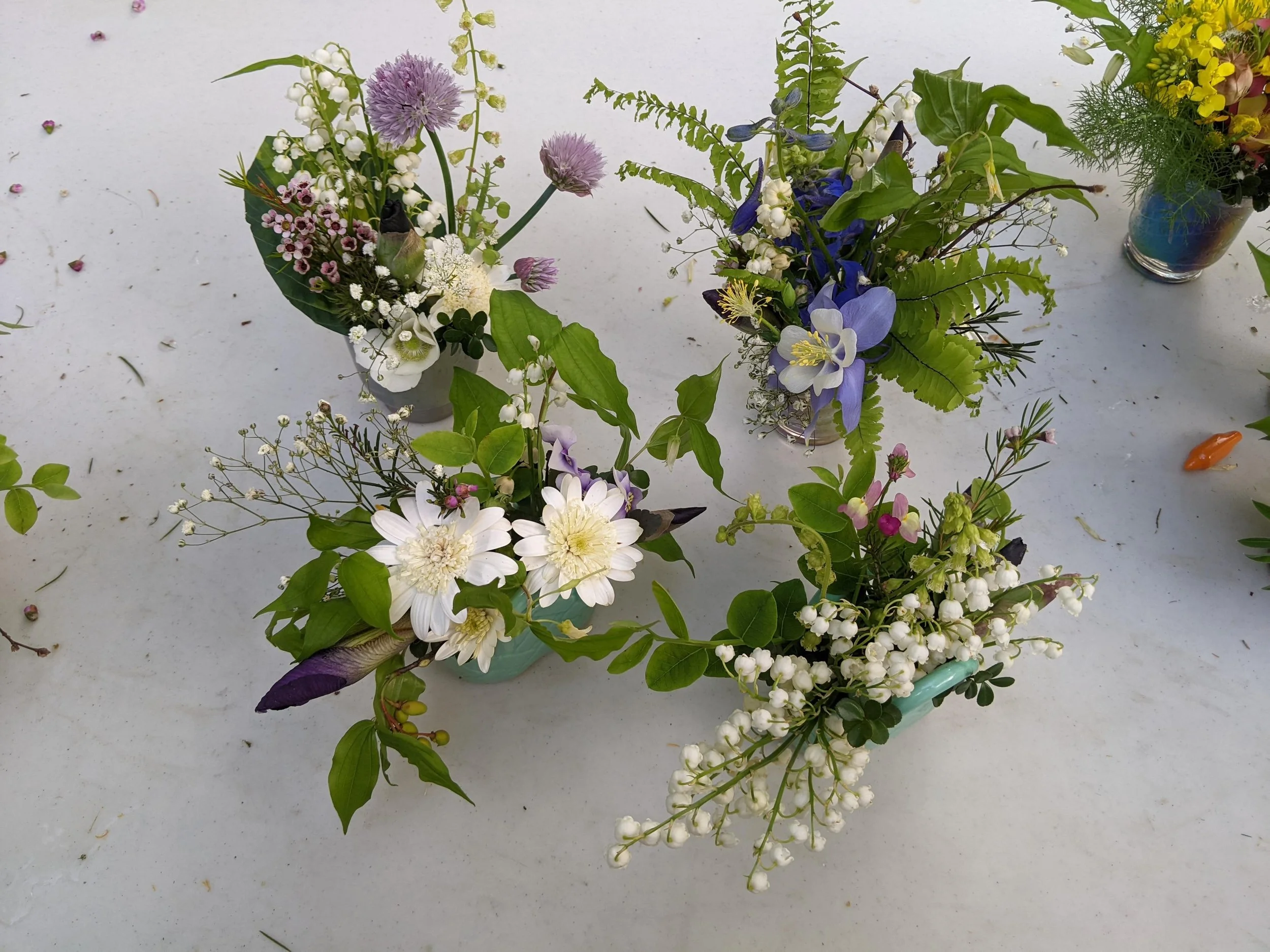 Arrangement of four floral centerpieces with white, purple, and pink flowers, and green foliage on a white surface.